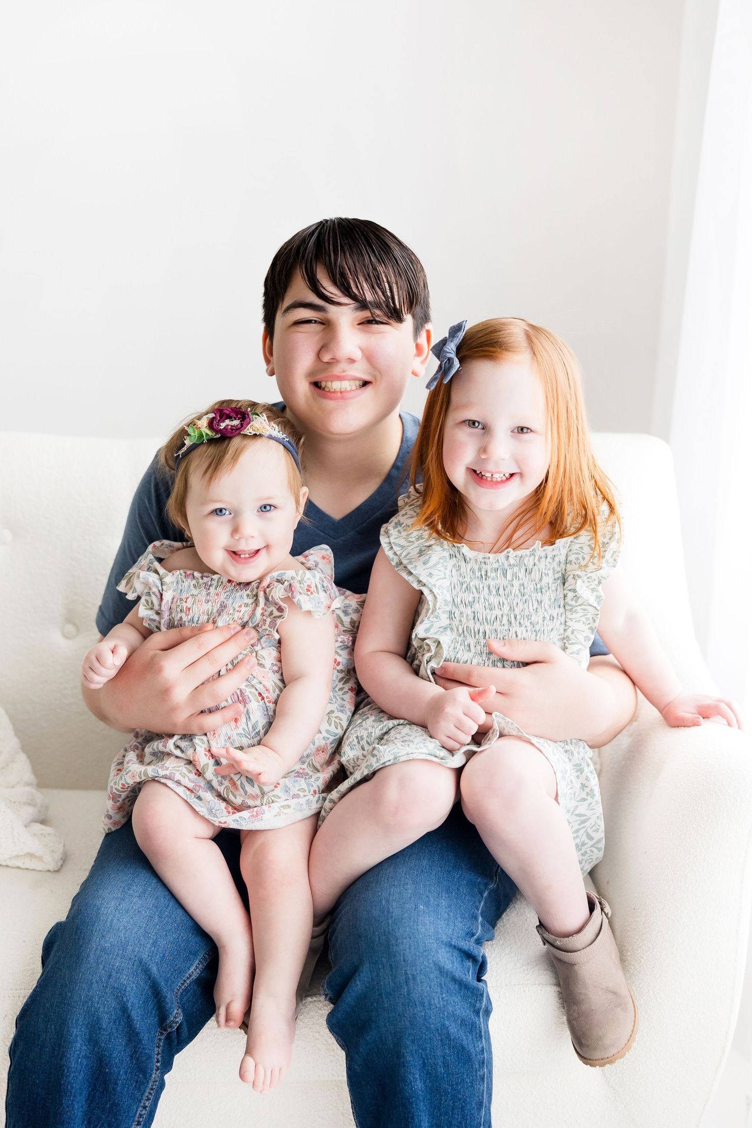 A family sits together on a white couch, wearing coordinated outfits in soft floral and cream colors.