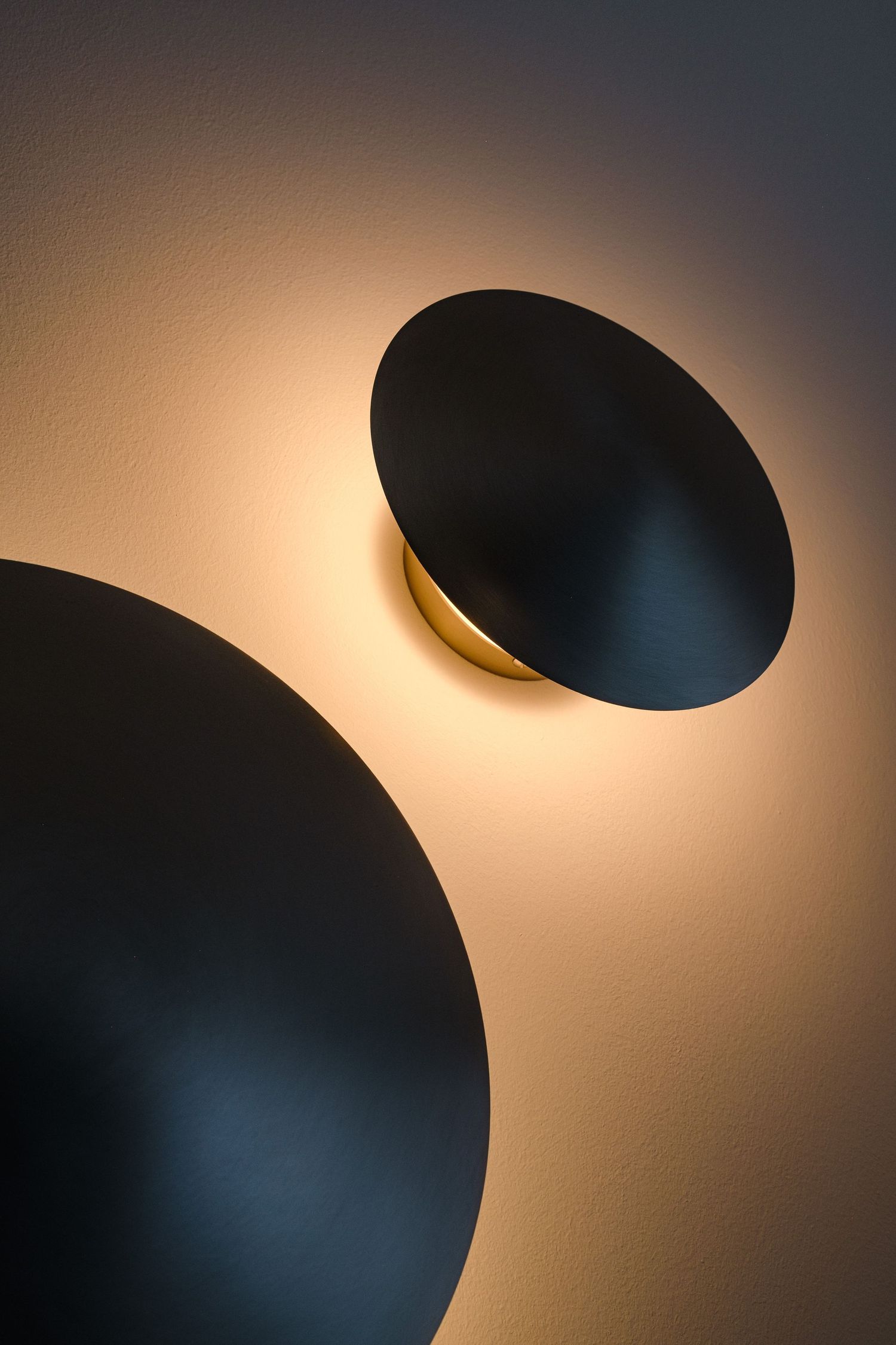 Abstract lighting installation with circular black shapes casting warm glows on wall.