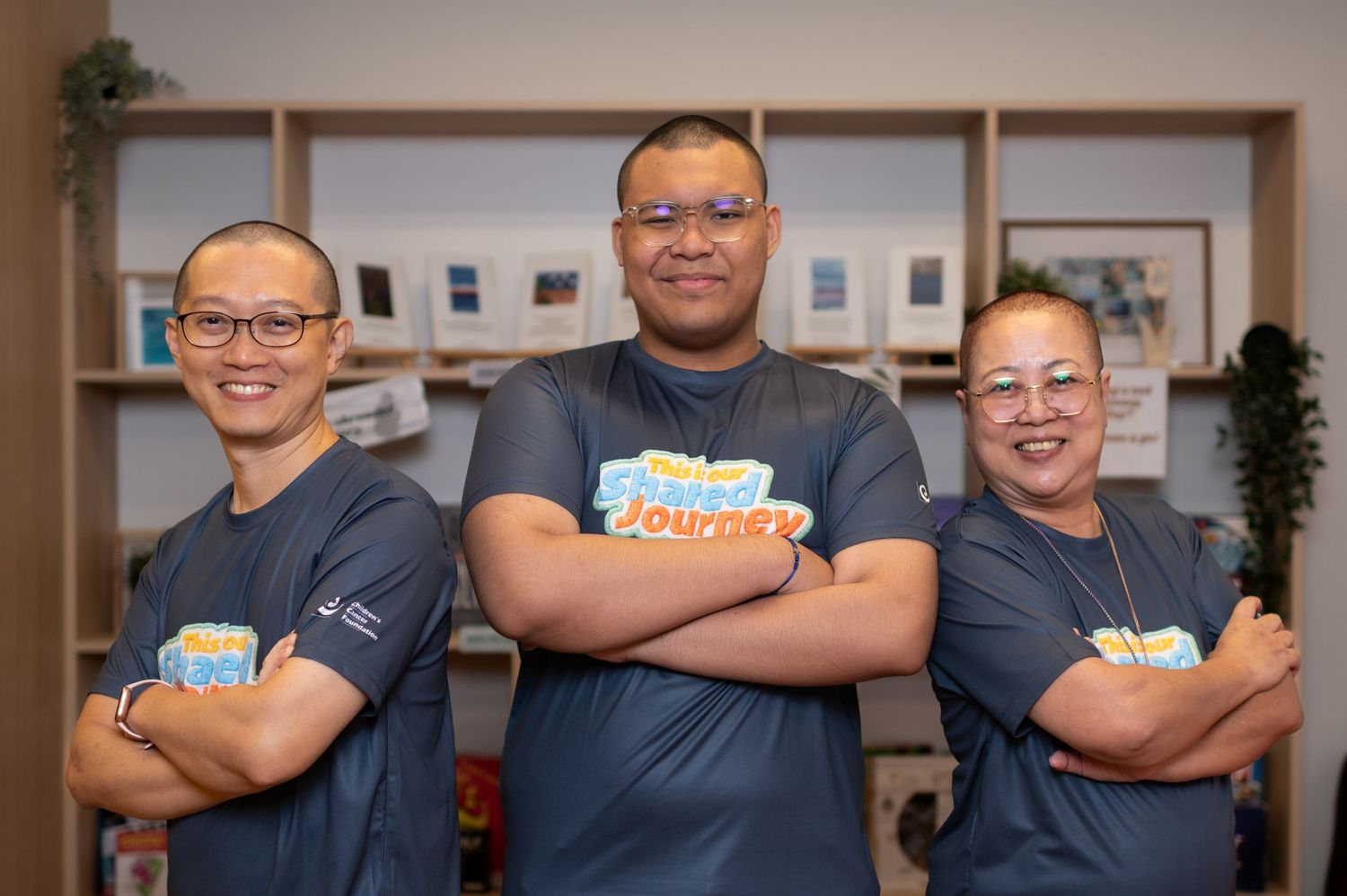 Three people in matching blue jerseys pose with arms crossed, smiling together indoors.
