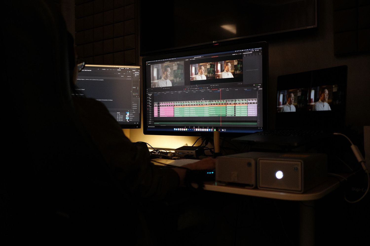 Dark editing suite with multiple computer monitors displaying video editing software.