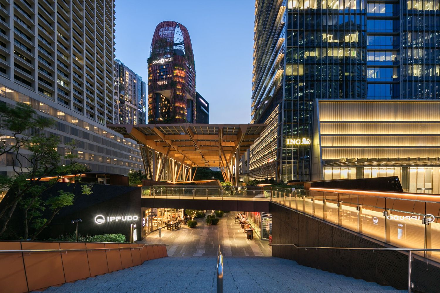 Modern office building exterior with glass facade and illuminated walkways at dusk.