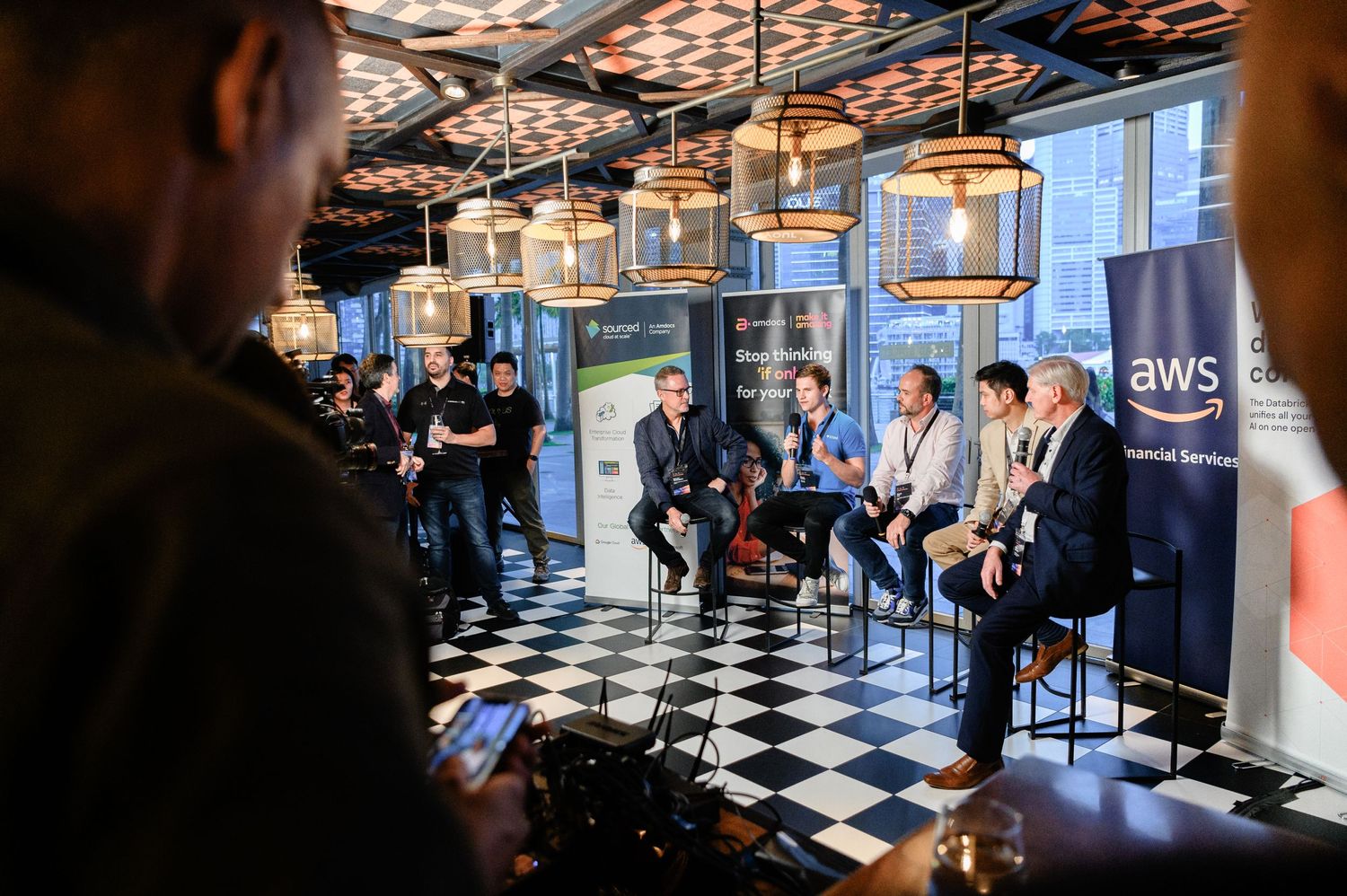 People gathered in a stylish bar area with checkered floor and modern lighting fixtures.