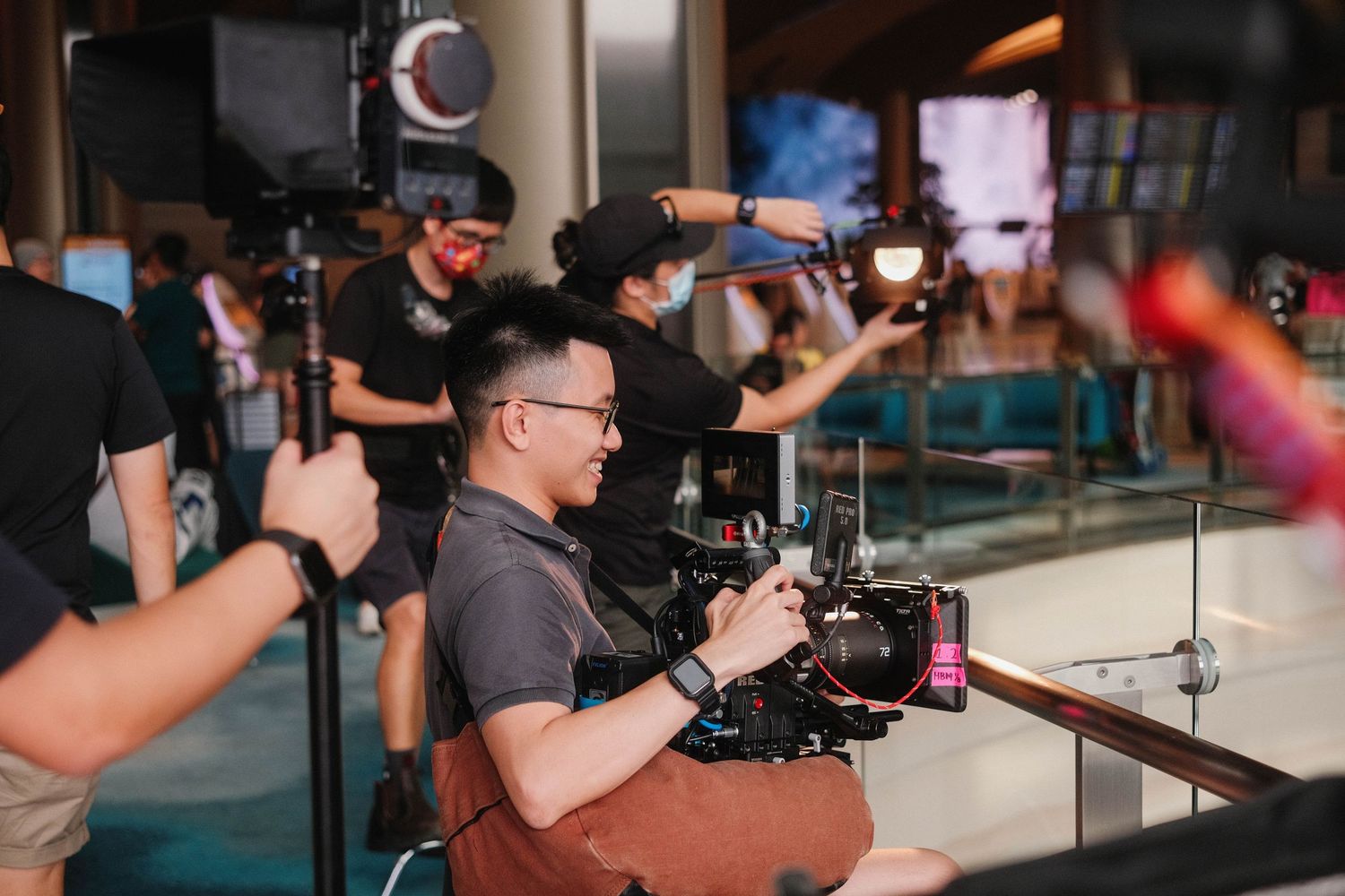 A film crew on a movie set with a cameraman holding a cinema camera while colleagues manage lighting equipment.