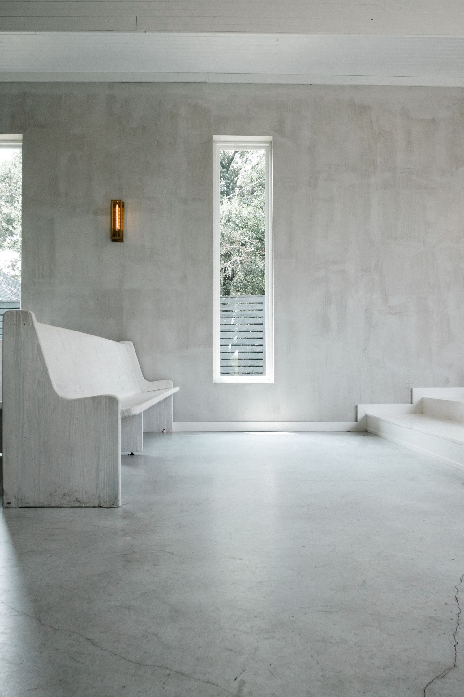 Minimalist white chapel interior with concrete walls, polished floors, white bench, and narrow windows.