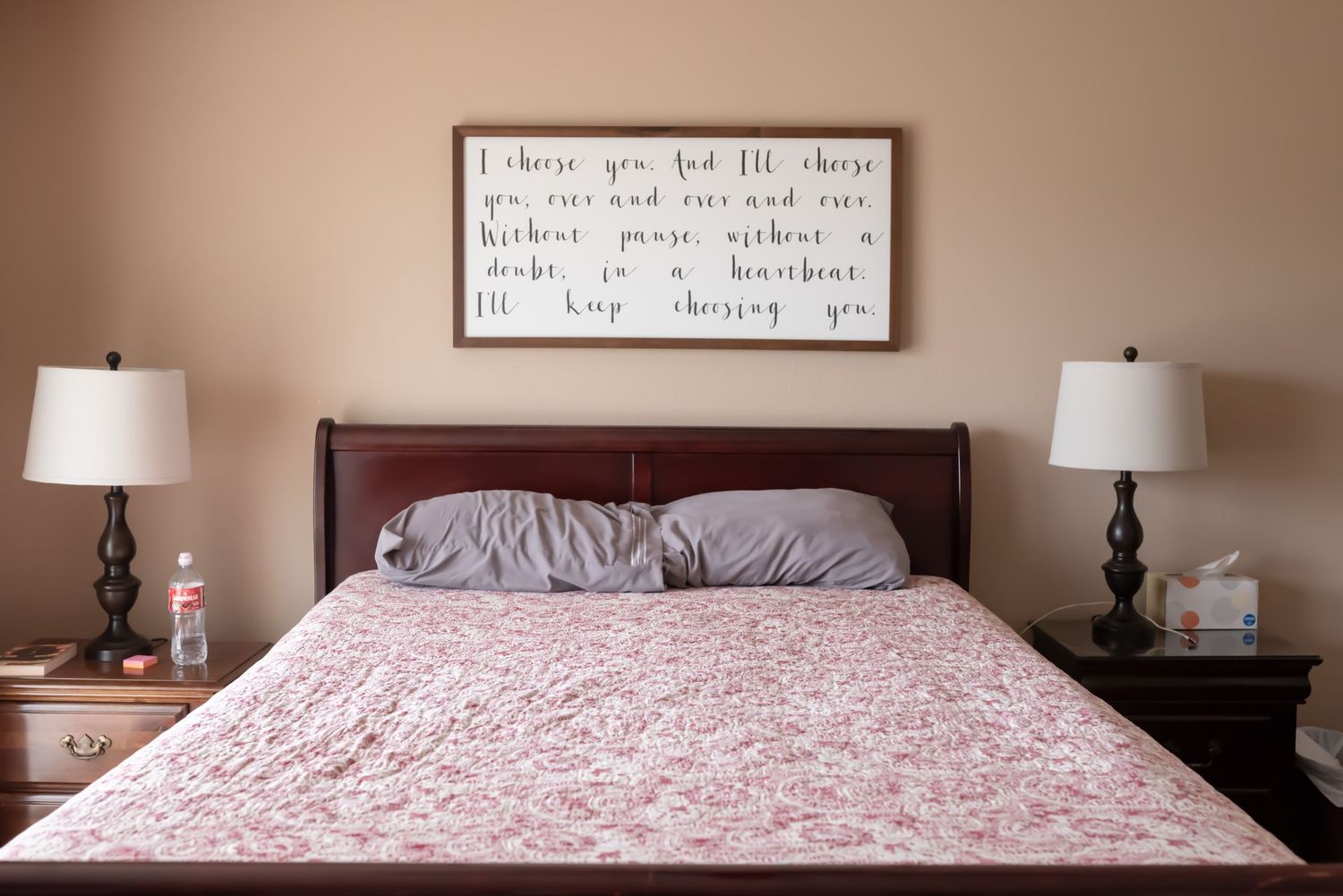 Queen sized bed with red quilt and flat grey pillows. End tables on either side are cluttered with items.  Doughman Photography.