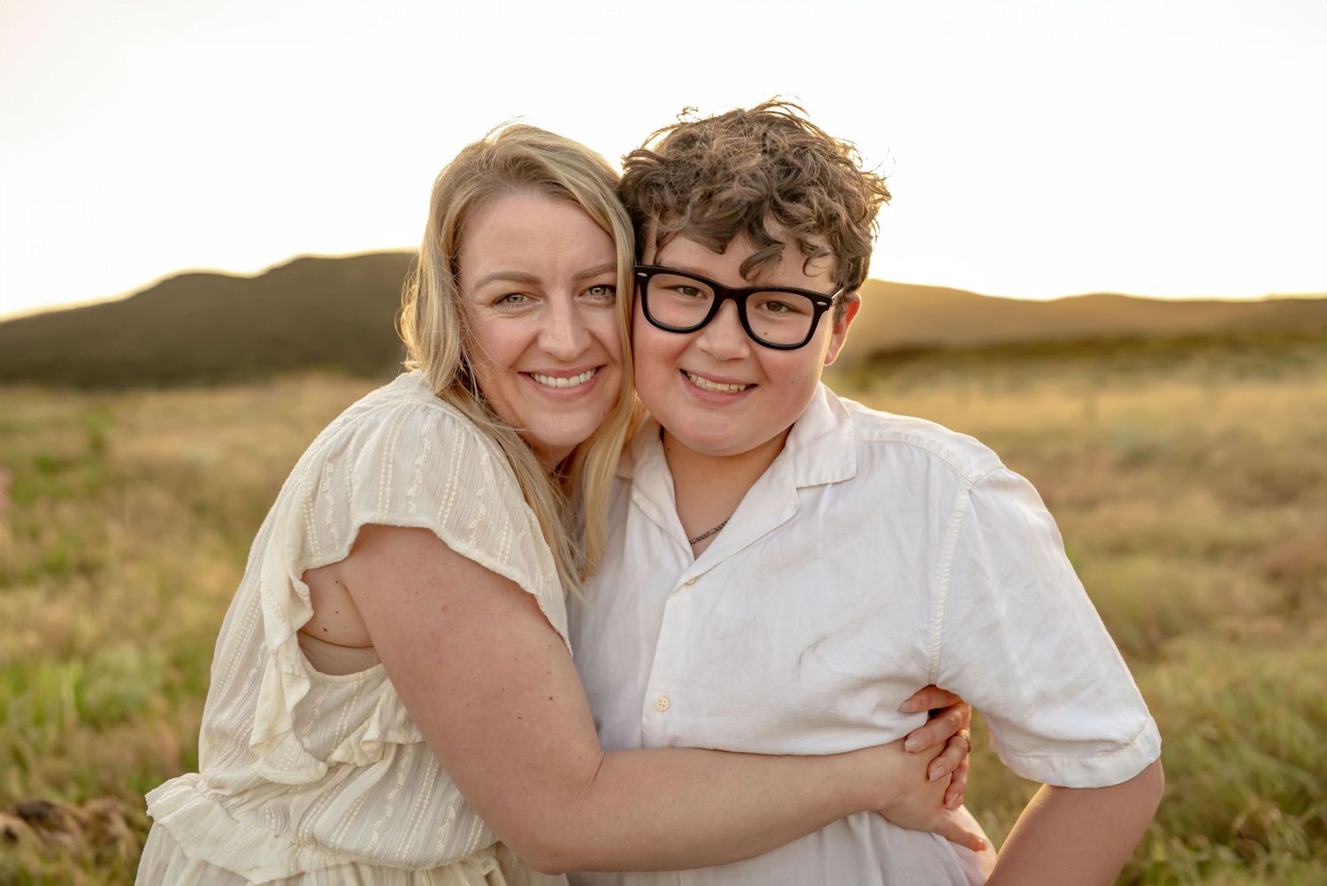 Mother hugging her teenage son in an open field on a bright sunny day. Doughman Photography