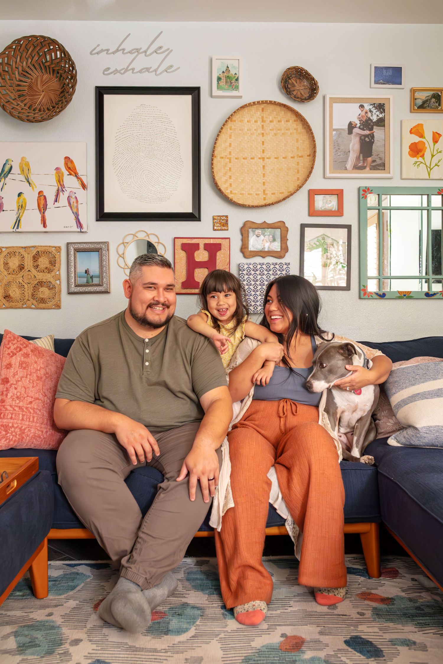 A smiling and happy family of three is sitting on the couch with their dog.  Doughman Photography