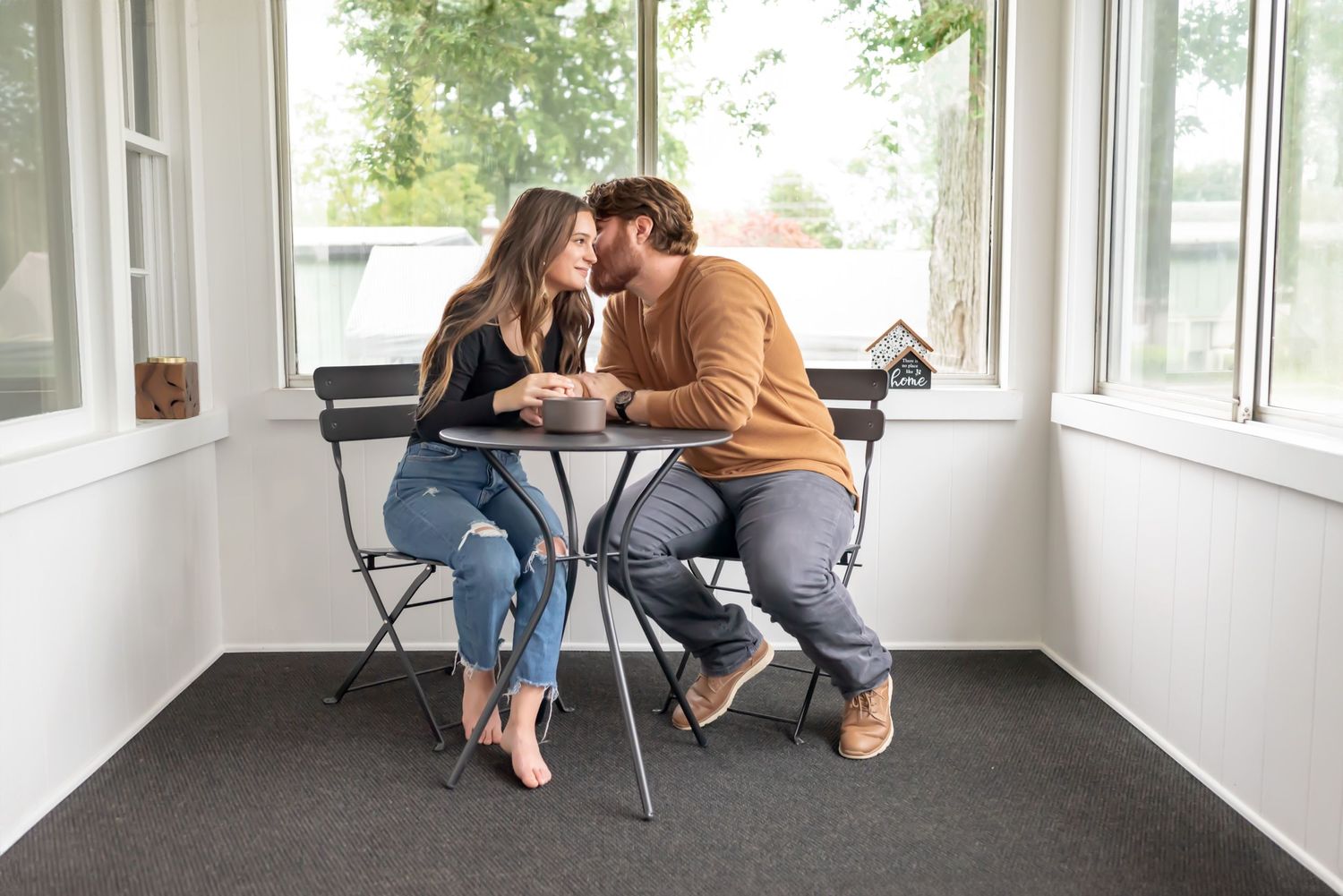 Couple sitting at bistro set. He whispers something in her ear. Doughman Photography.