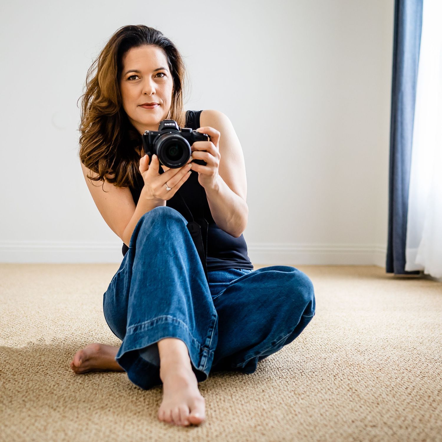 Self portrait of Karen Doughman sitting on the floor posed to take a picture with her Nikon camera.  Doughman Photography