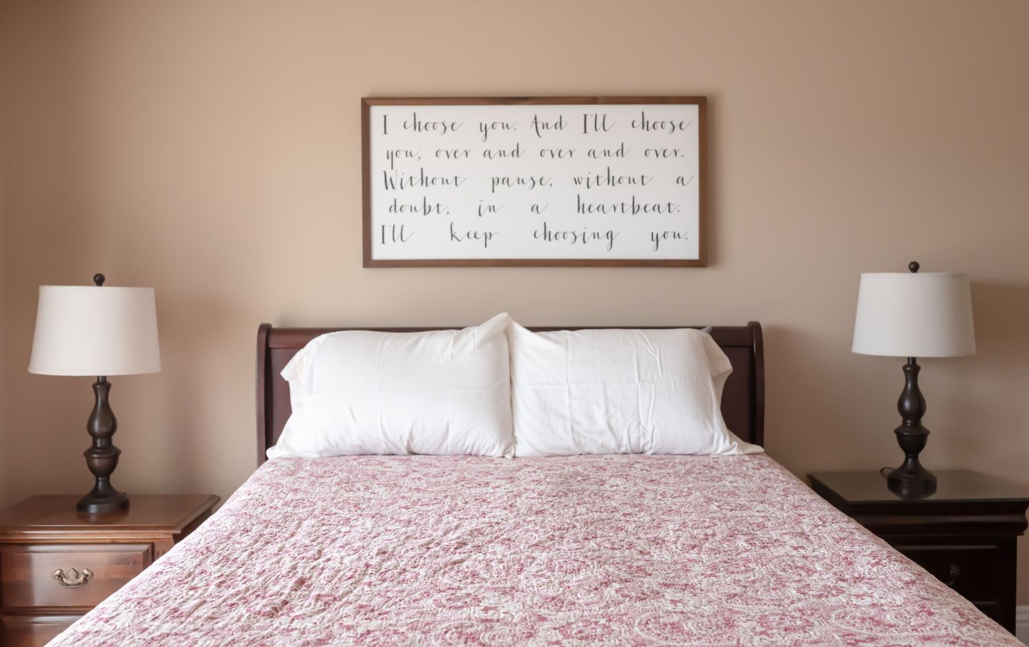 Queen sized bed with red quilt and large white pillows. Matching lamps and end tables on either side. Doughman Photography.