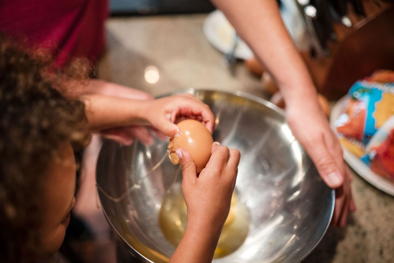 Close up of toddler hands cracking eggs while mom holds the bowl. Doughman Photography.