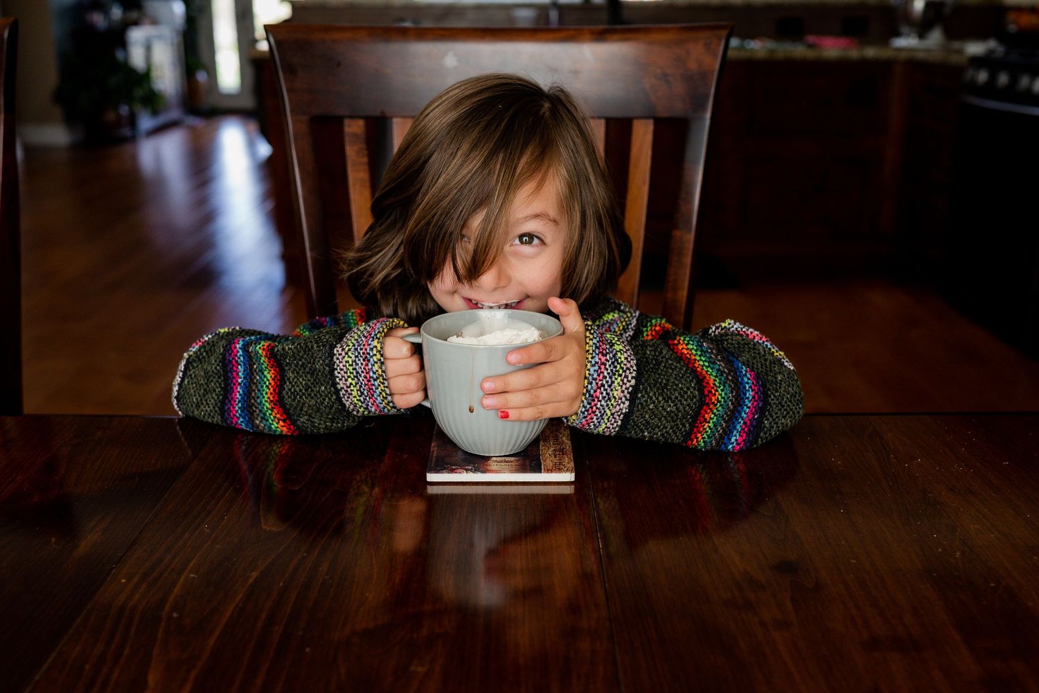 Young child making eye contact with the camera while sipping hot chocolate with whipped cream.  Doughman Photography.