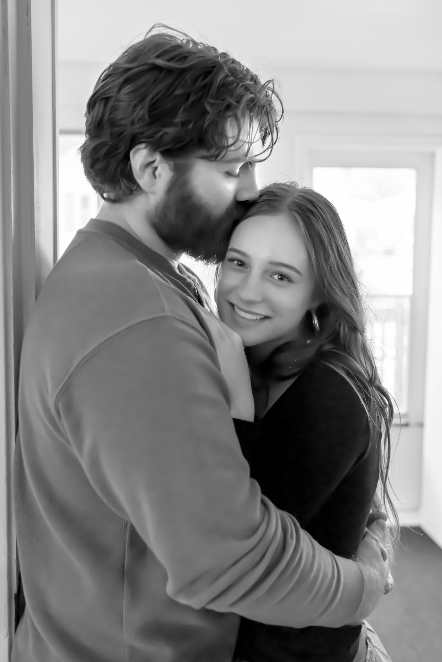 Couple standing in a doorway. The man is kissing her forehead while she looks directly into the camera. Doughman Photography