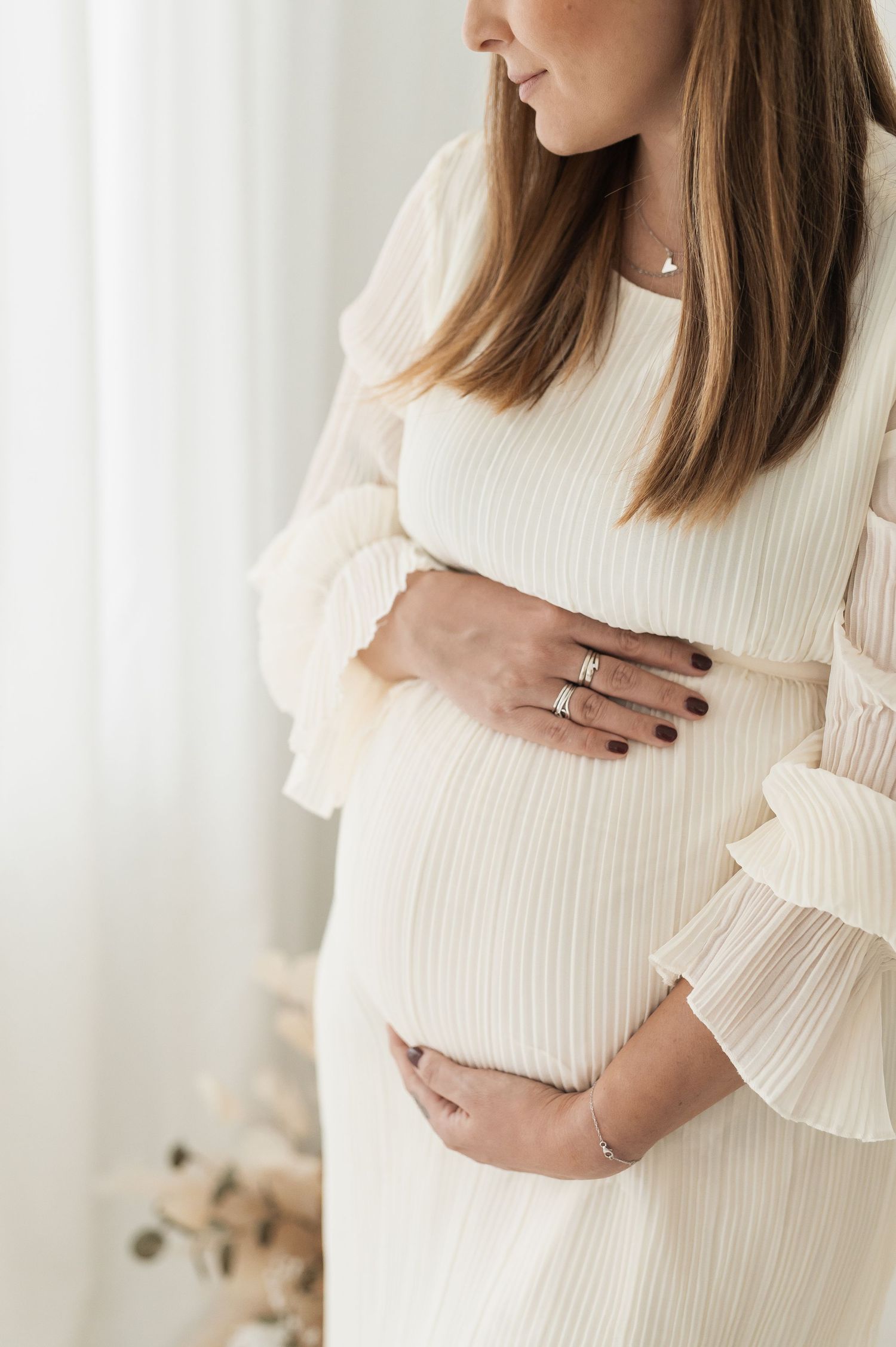 Close-up shots of pregnant woman in cream sweater gently cradling her baby bump against light background.