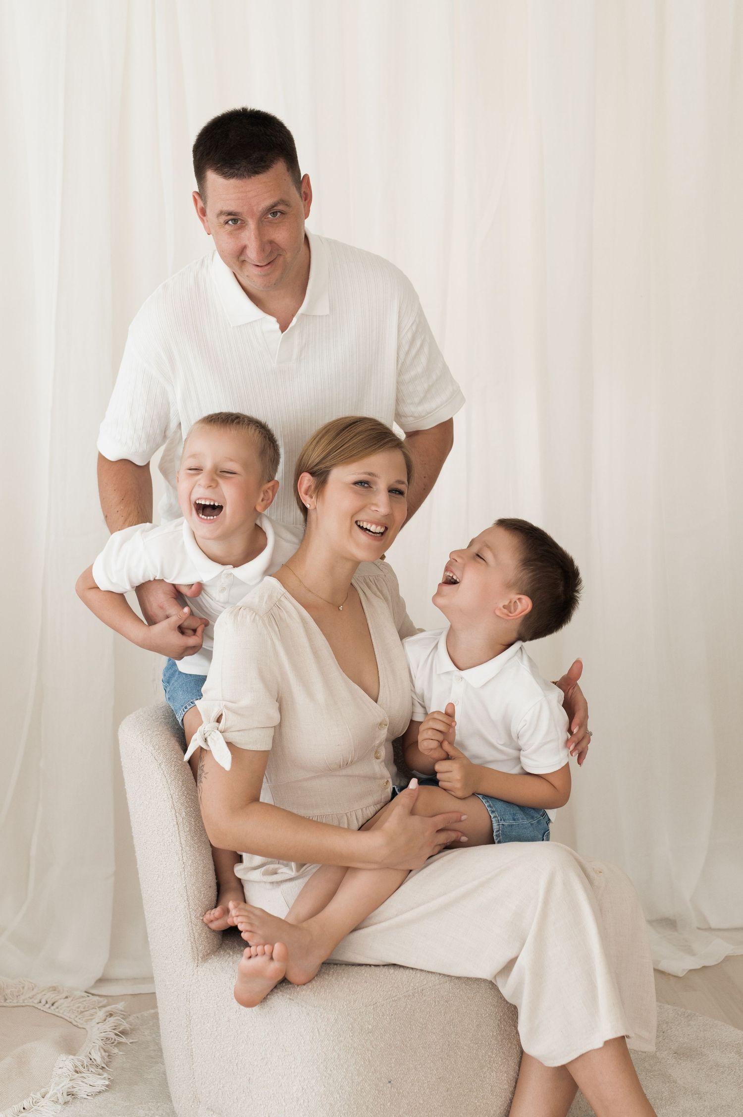 Family wearing white clothing embraces and laughs together joyfully during indoor photo session.