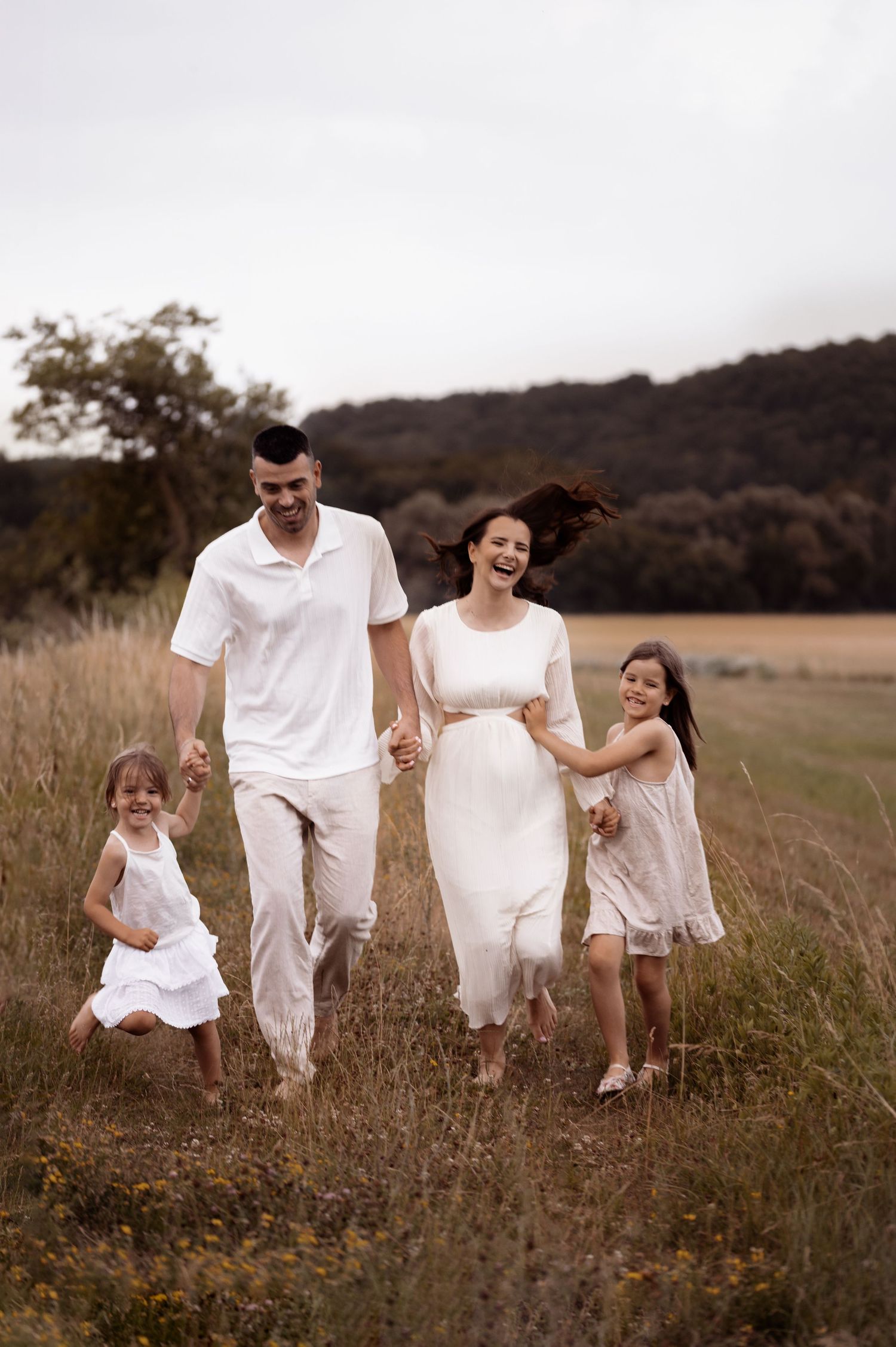 A family in white outfits walks together holding hands through a serene meadow at sunset.