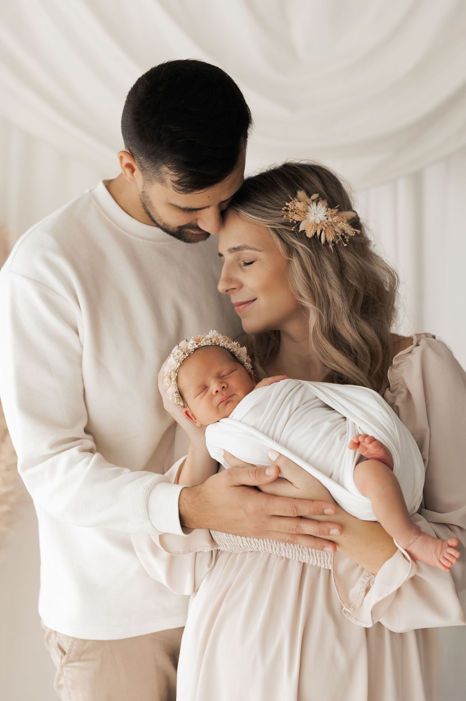 Tender family moments captured in a series of soft white newborn photography portraits showing parents embracing their baby.