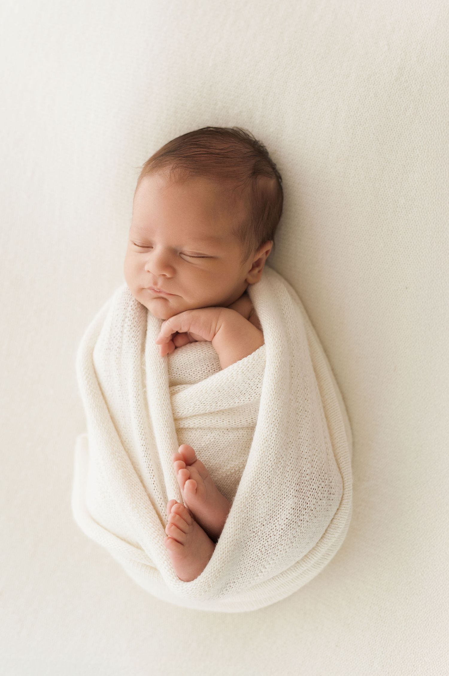 A sleeping newborn baby wrapped in soft white blankets shown from different angles in a minimal style photo series.