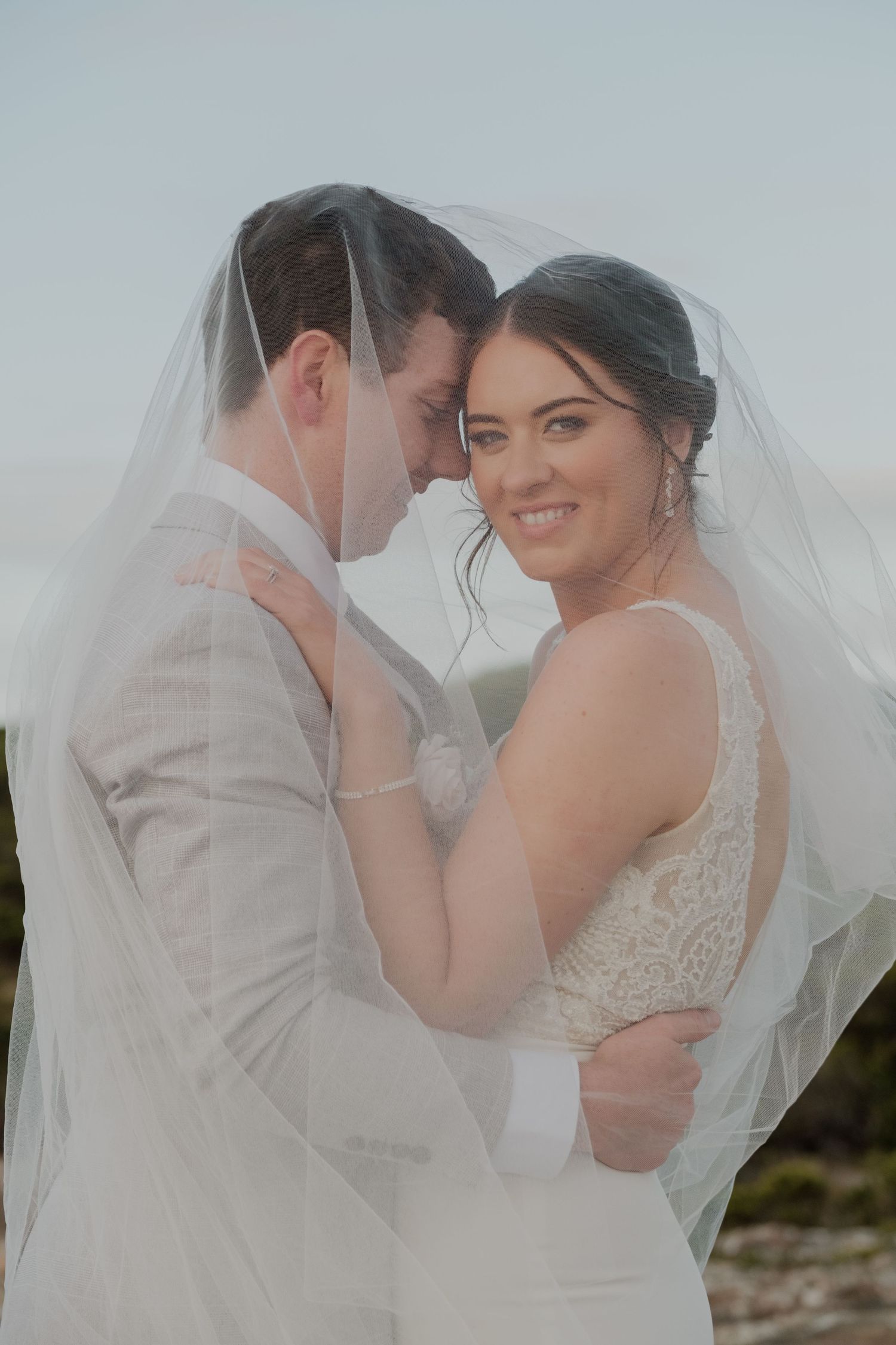 Romantic wedding portrait with couple embracing under a flowing veil.