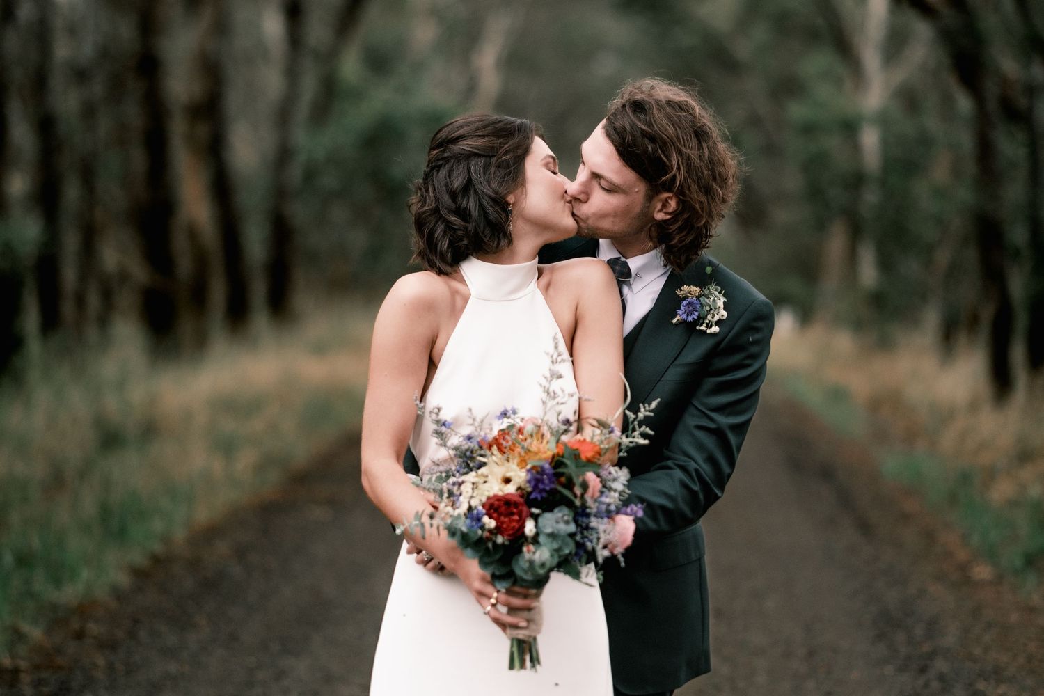 A romantic wedding couple embracing on a tree-lined path in autumn.
