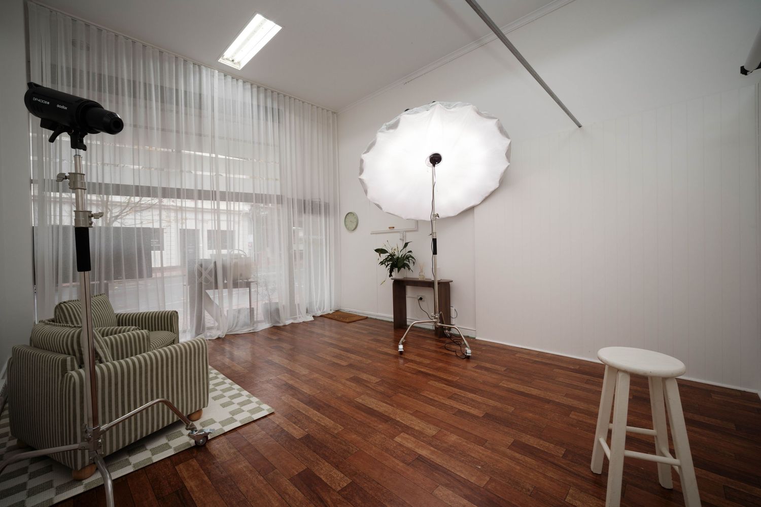 Bright photography studio with hardwood floors, white umbrella light, sheer curtains, and minimalist decor.