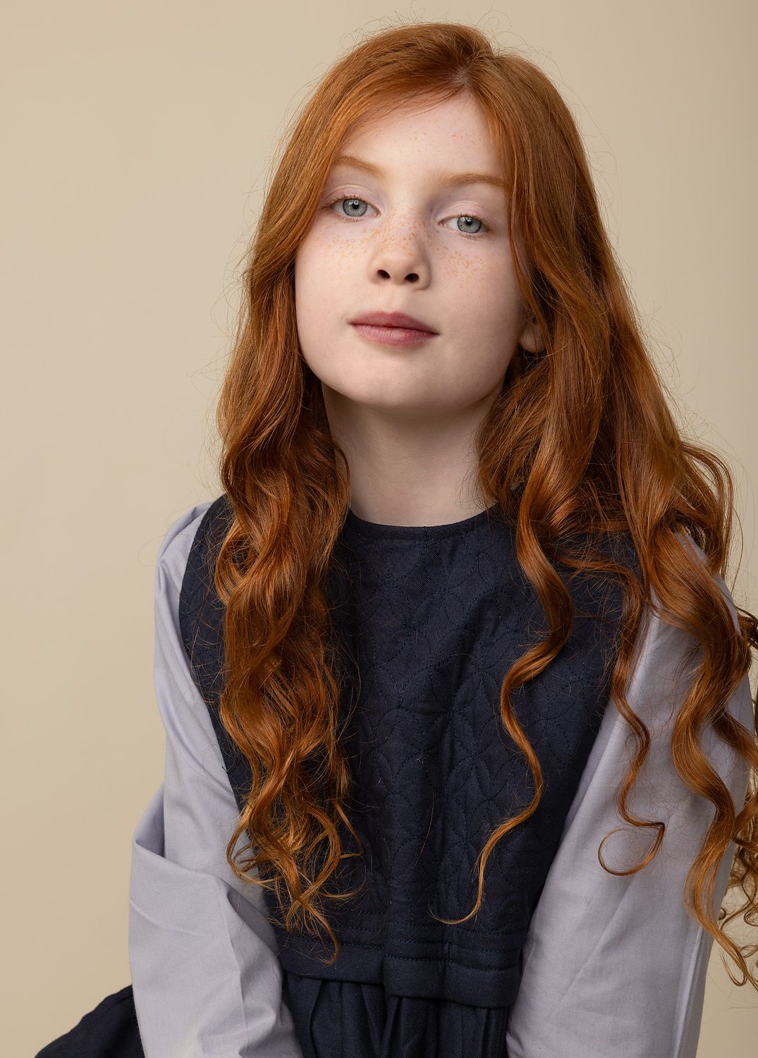 Young girl with long red curly hair wearing a cute navy dress posing for a model update shoot.