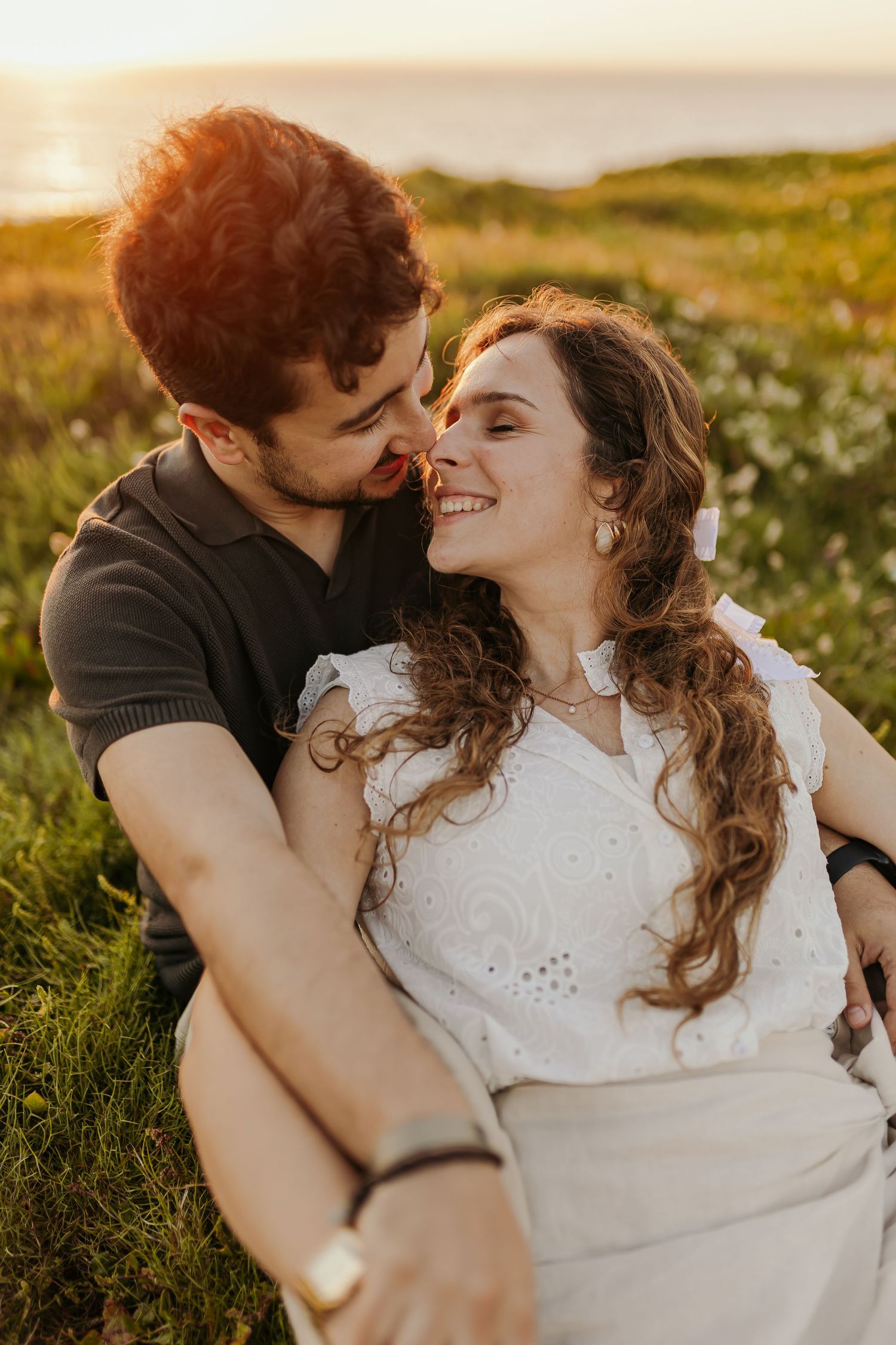 Couple sharing a romantic moment at sunset in a green meadow, woman smiling joyfully in white top.