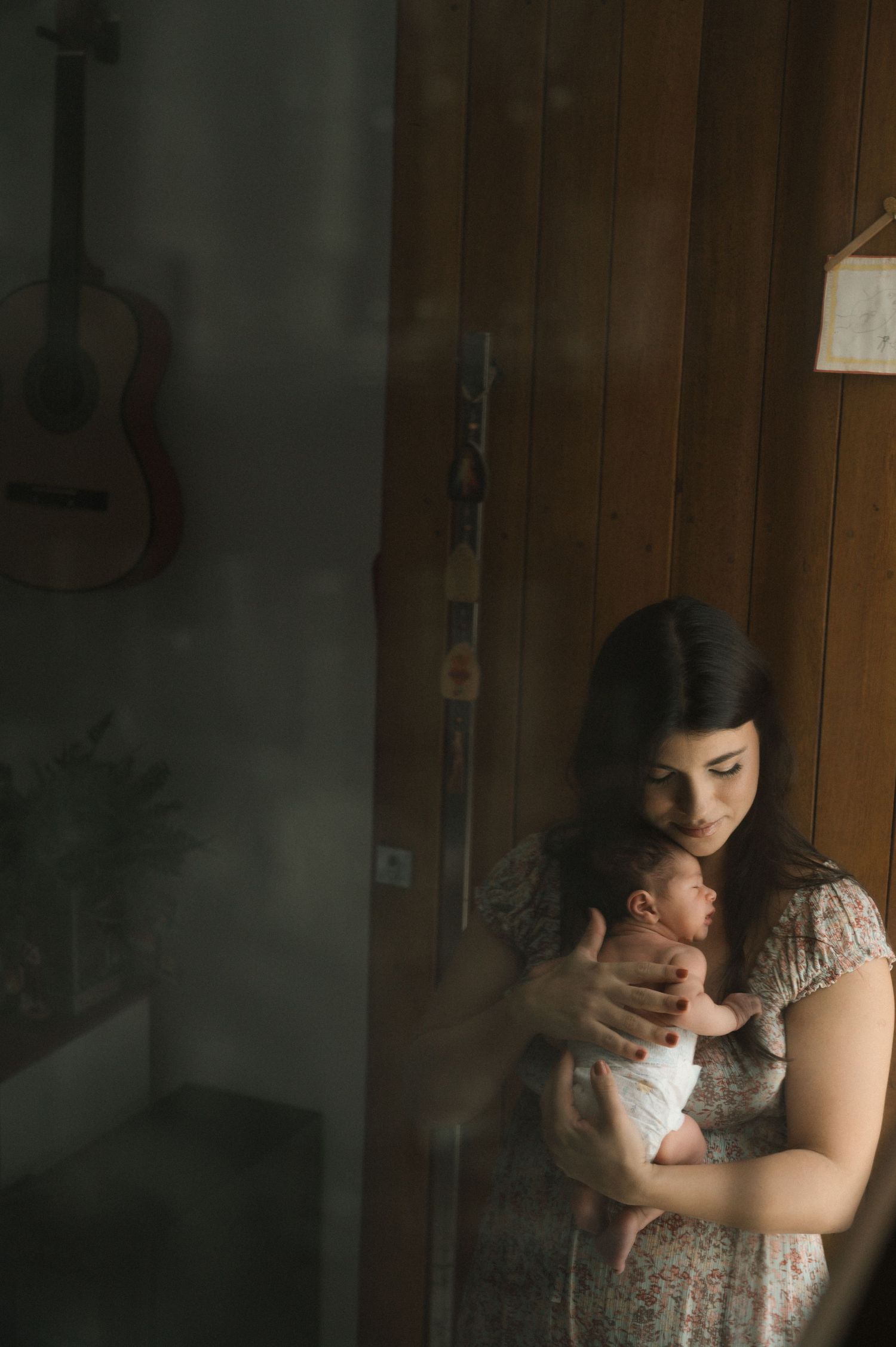 A tender moment captured in moody lighting through a window as a parent embraces their young child.