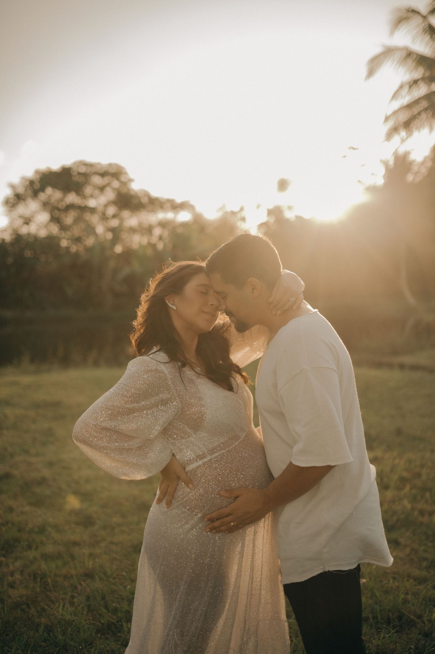 Romantic maternity photo of couple embracing during golden hour with palm trees in background.