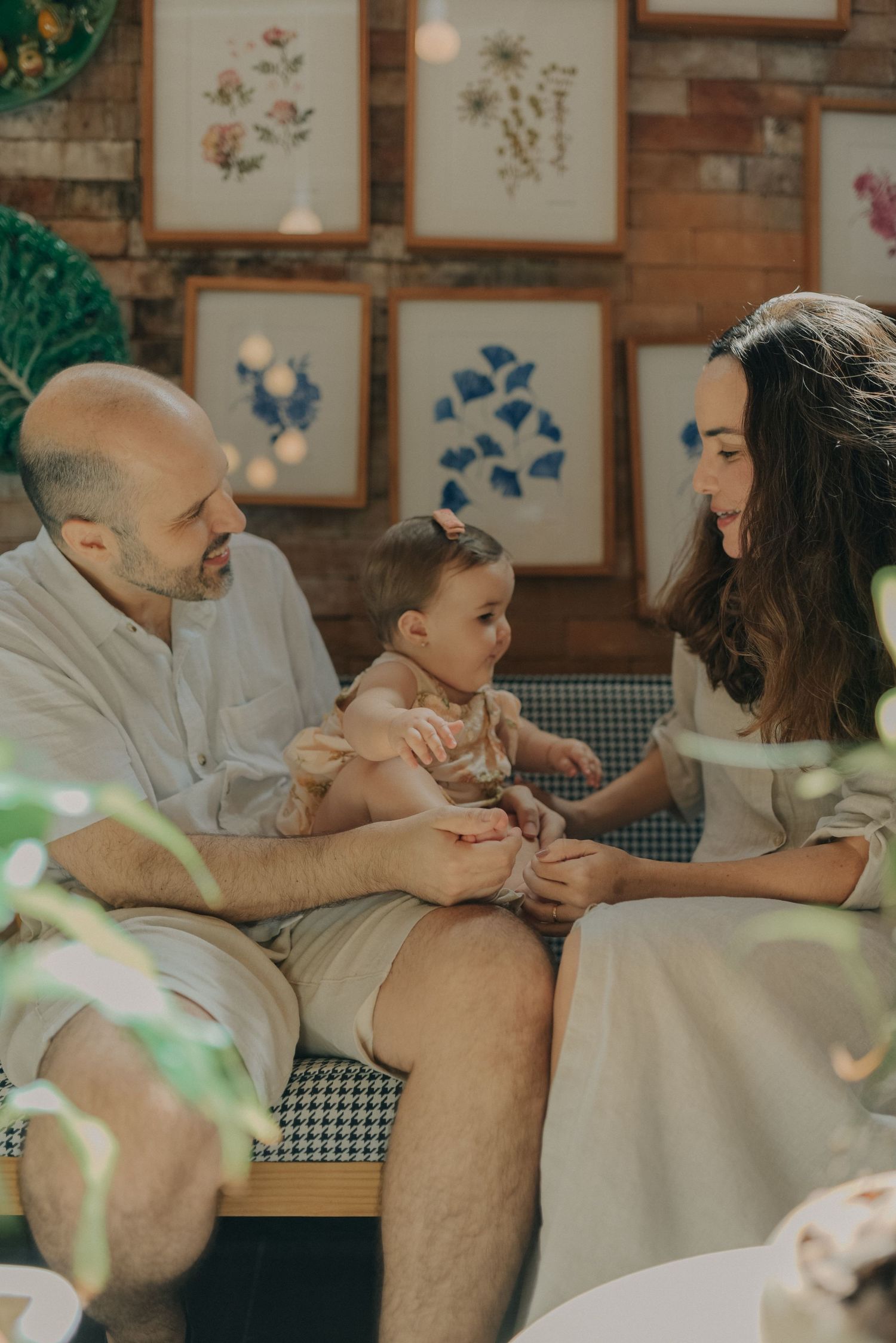Family sharing an intimate moment on a couch with botanical artwork displayed on brick wall behind them.