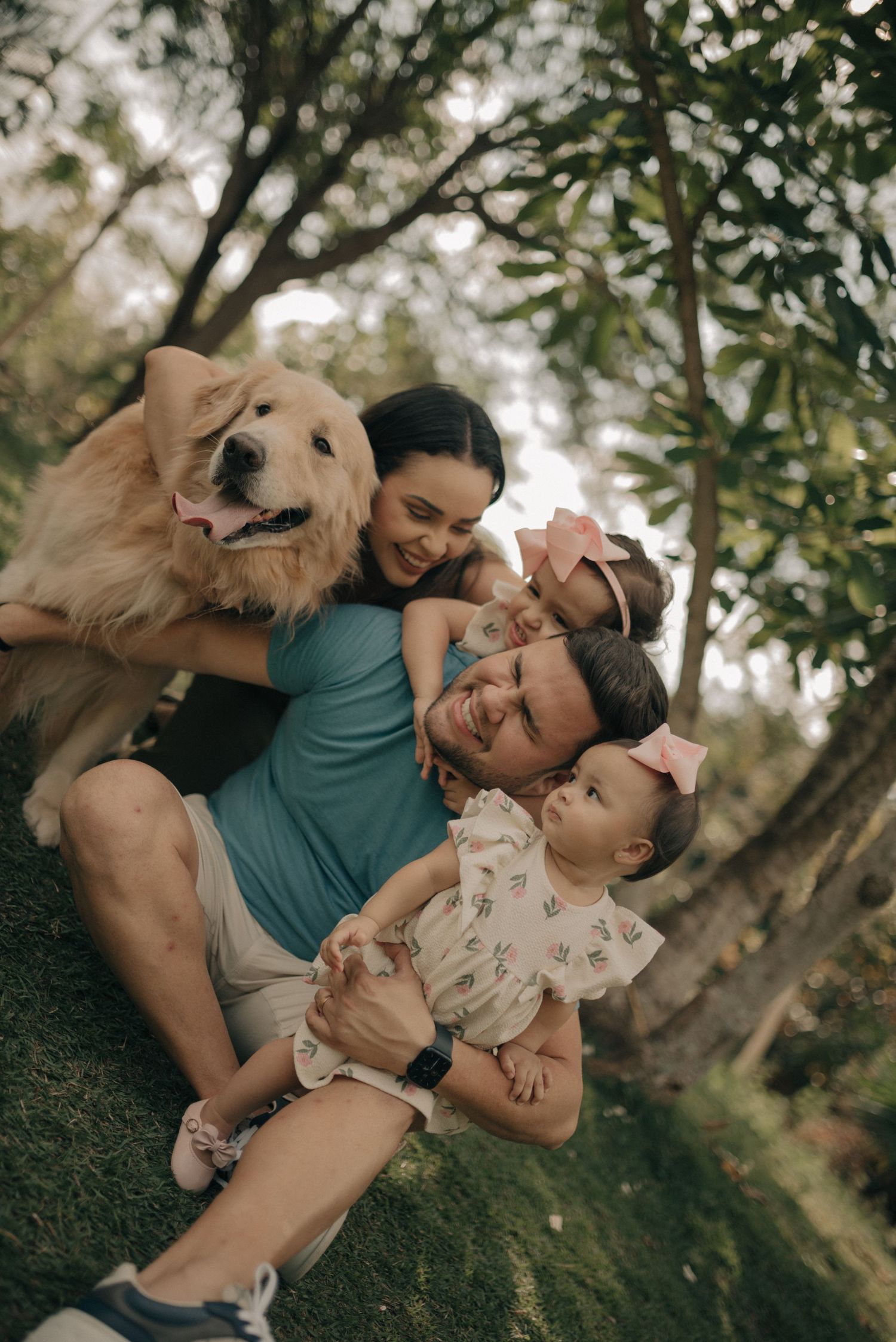 Happy family and Golden Retriever dog playing together outdoors under trees.