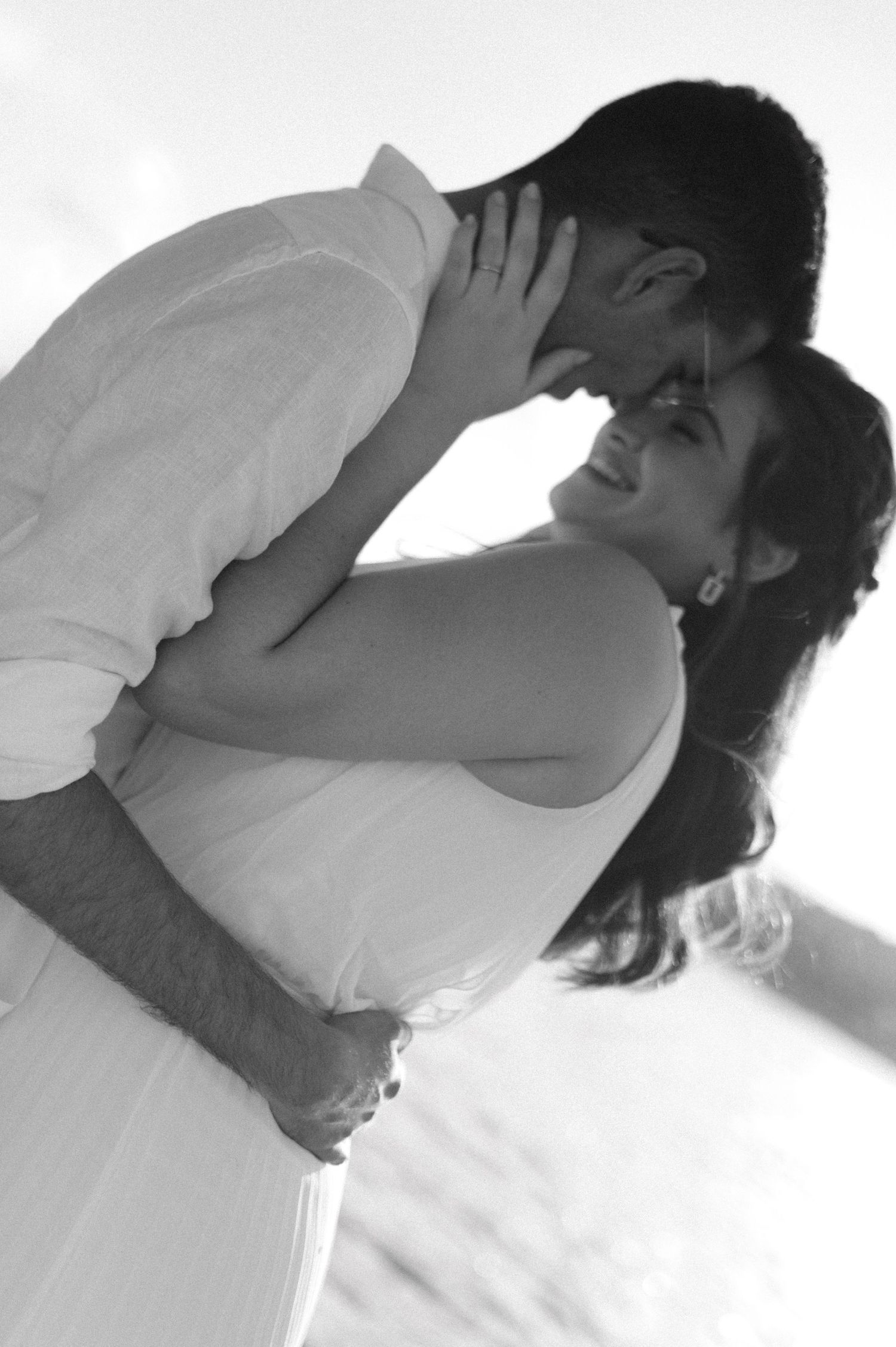 Intimate black and white portrait of couple in white clothing embracing with tender emotional connection.