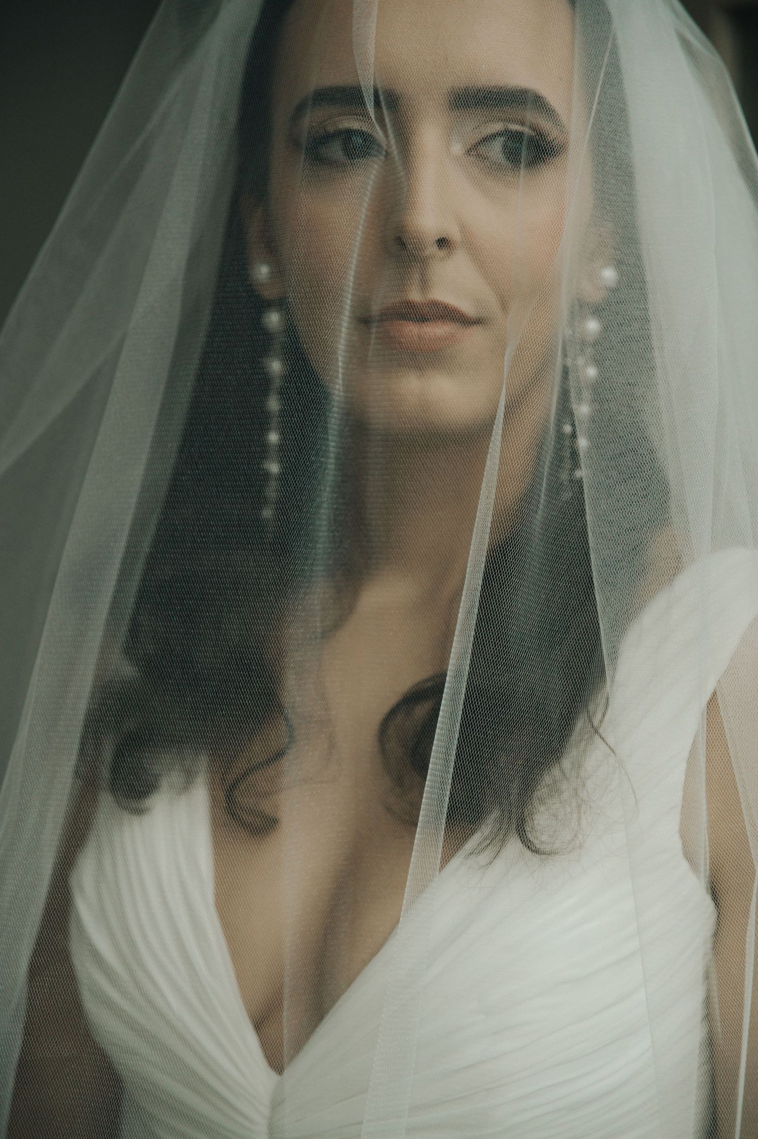 A bride in a white wedding dress and veil poses for a series of close-up portraits with dramatic lighting.