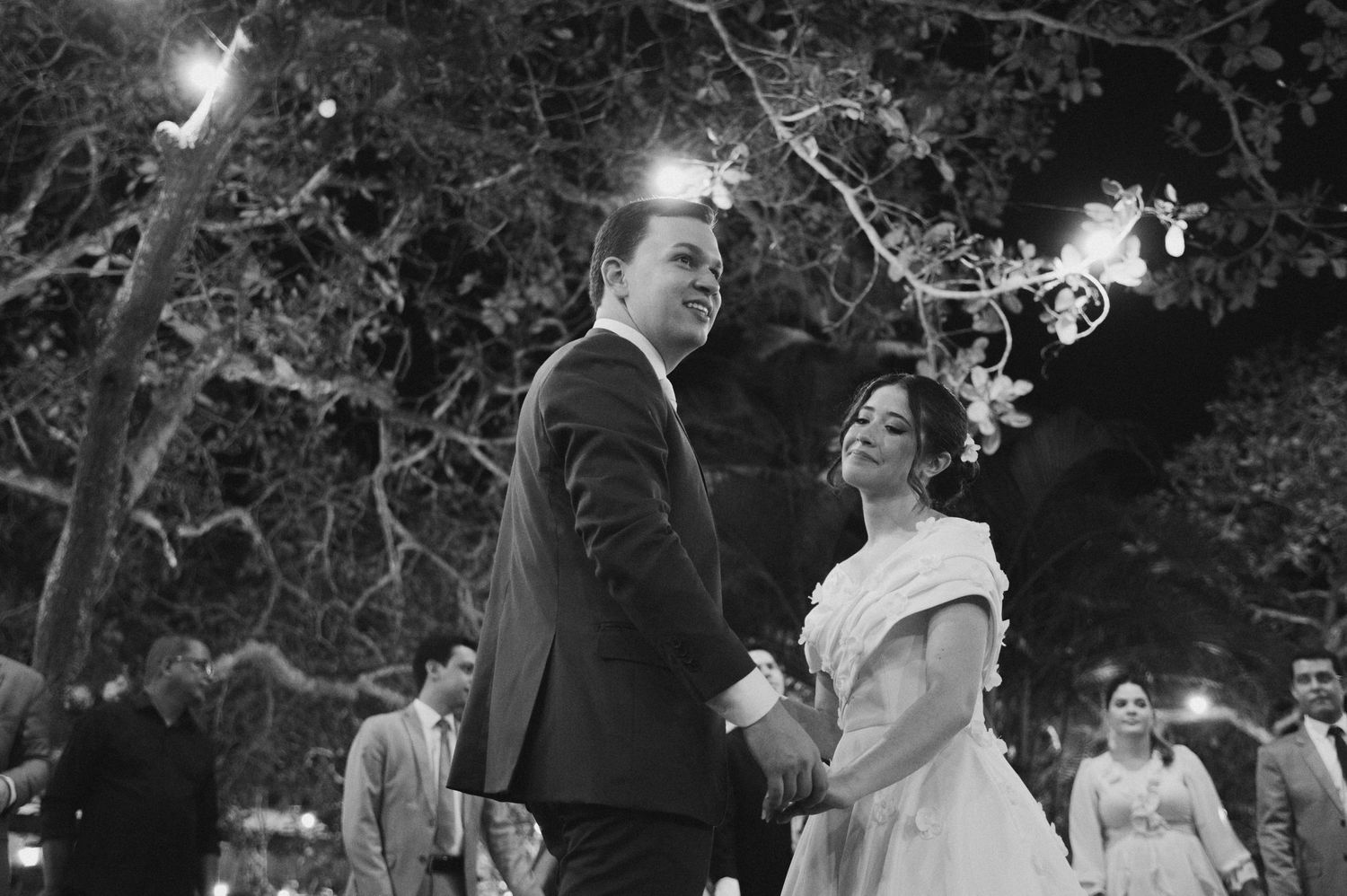 A classic black and white wedding dance moment captured under evening trees.