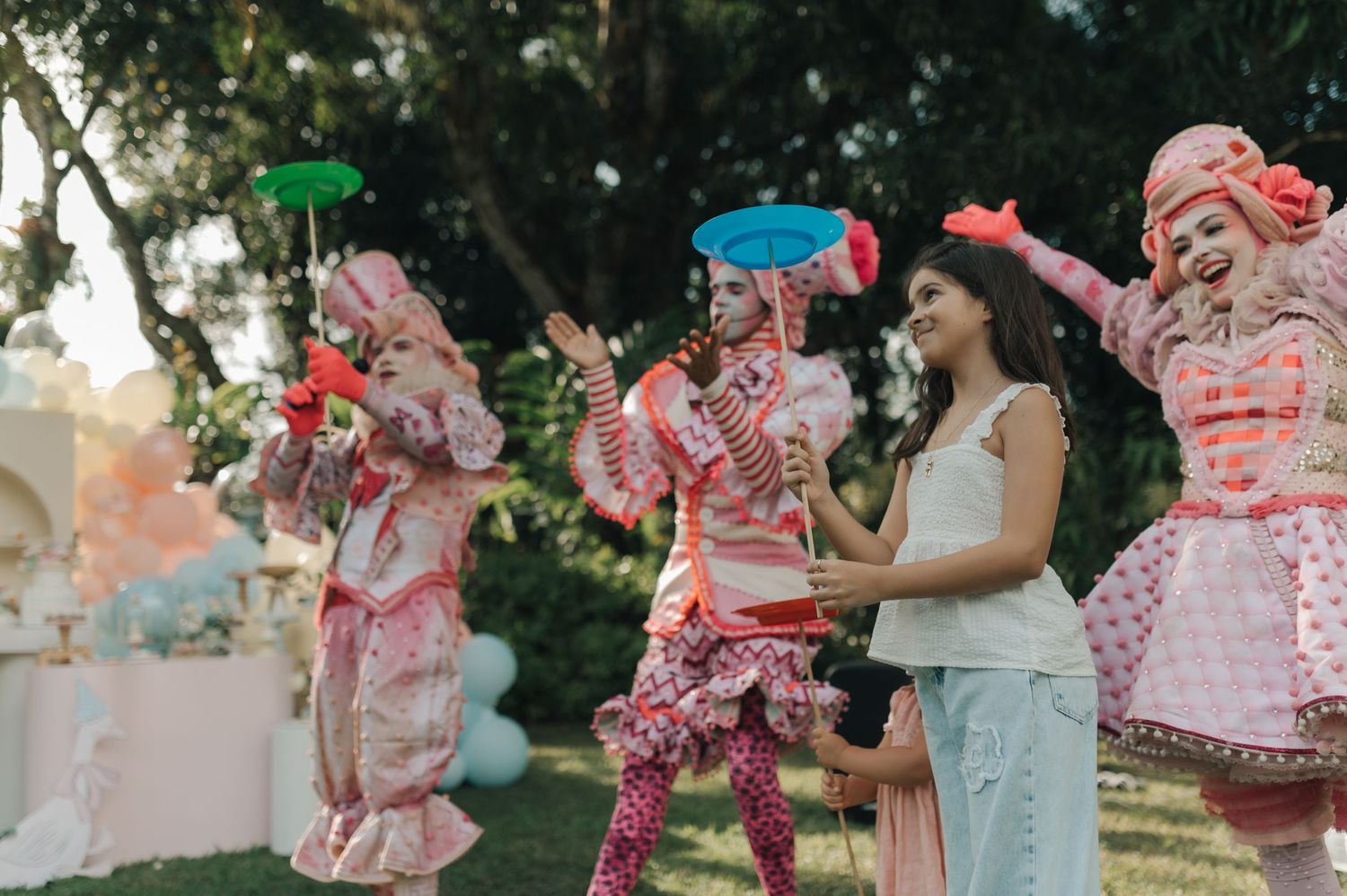 Costumed performers in pink outfits entertain guests at an outdoor party setting.