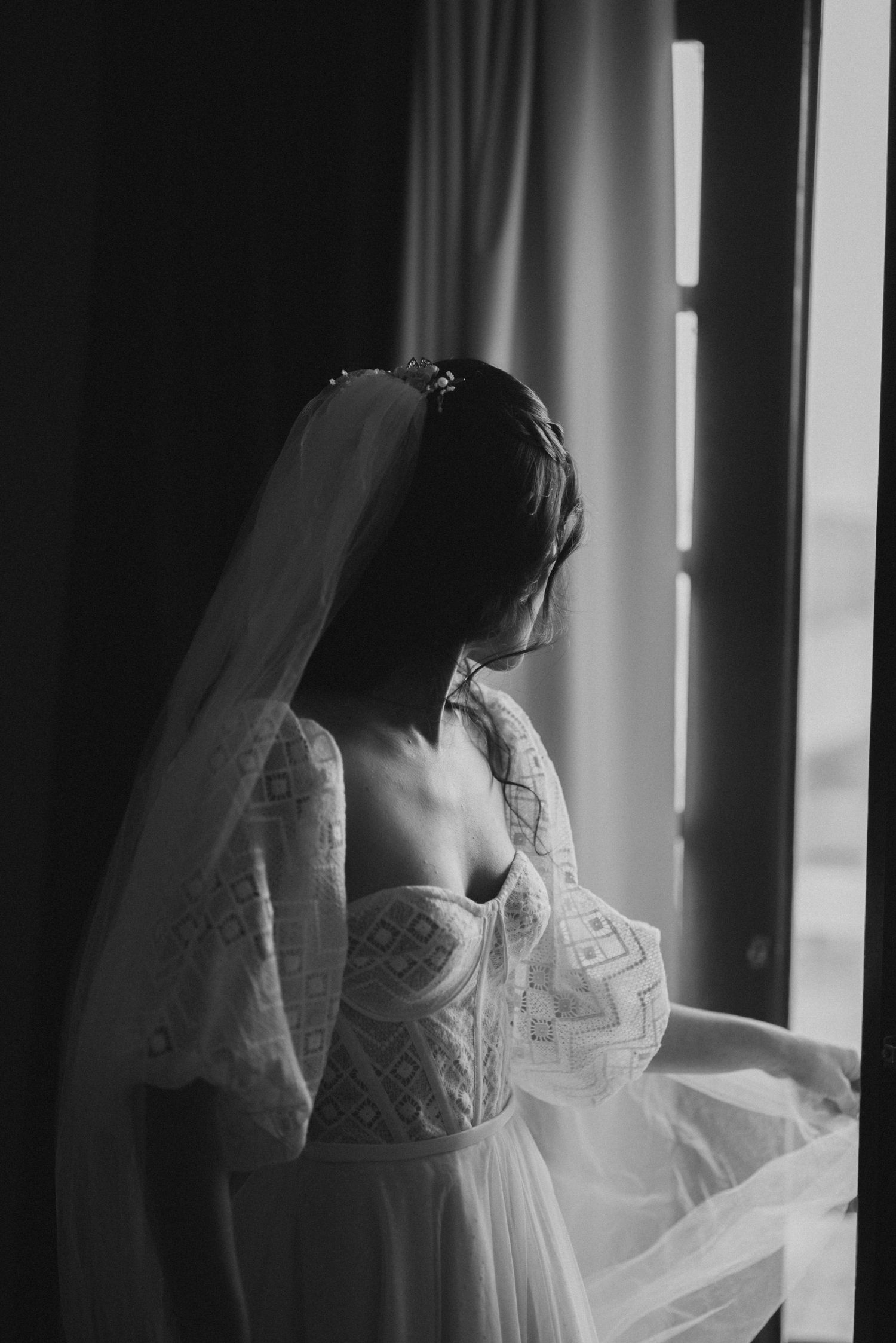 Silhouette of a bride in a corset dress standing by a window in dramatic lighting.