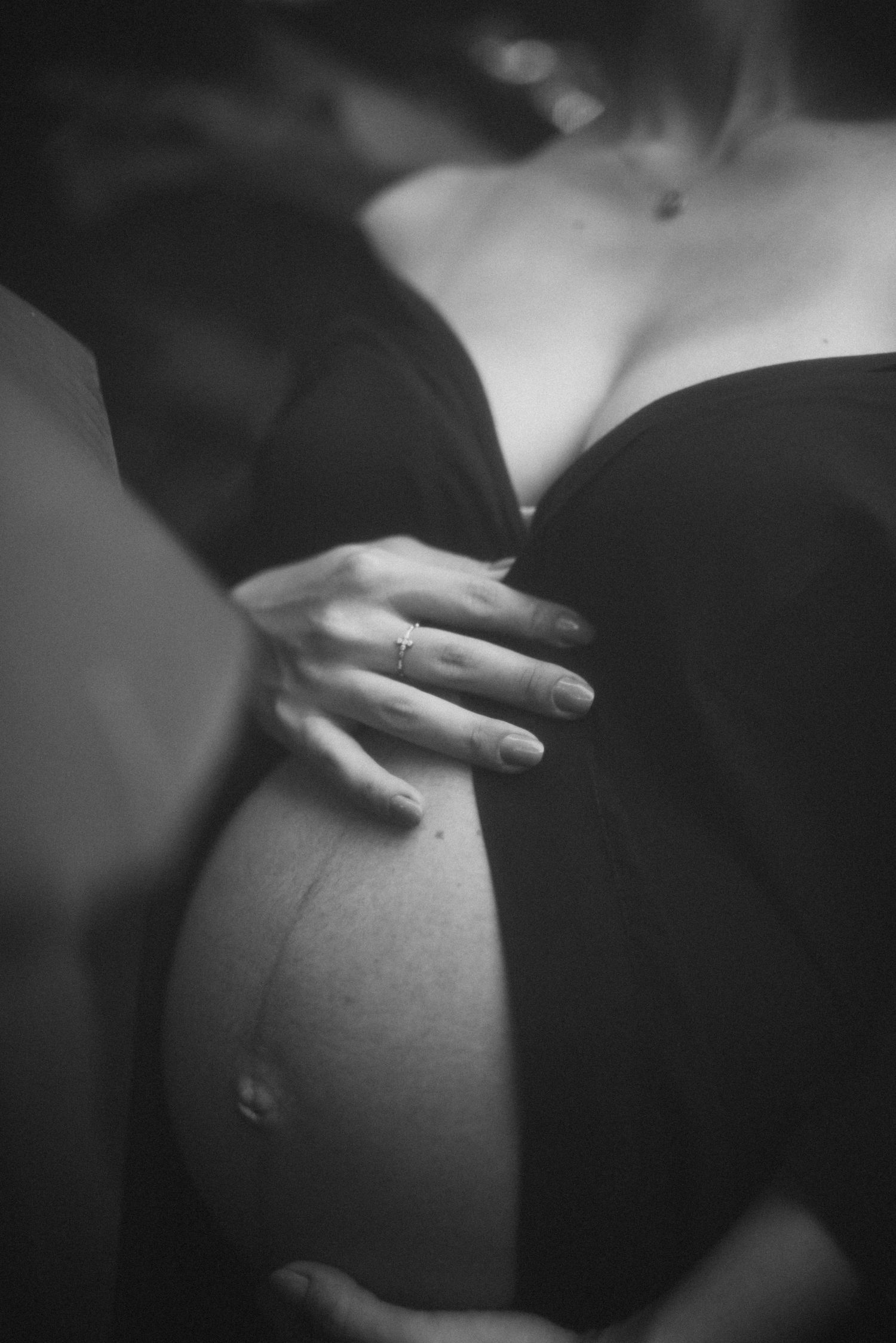 Intimate black and white close-up of hands cradling pregnant belly.