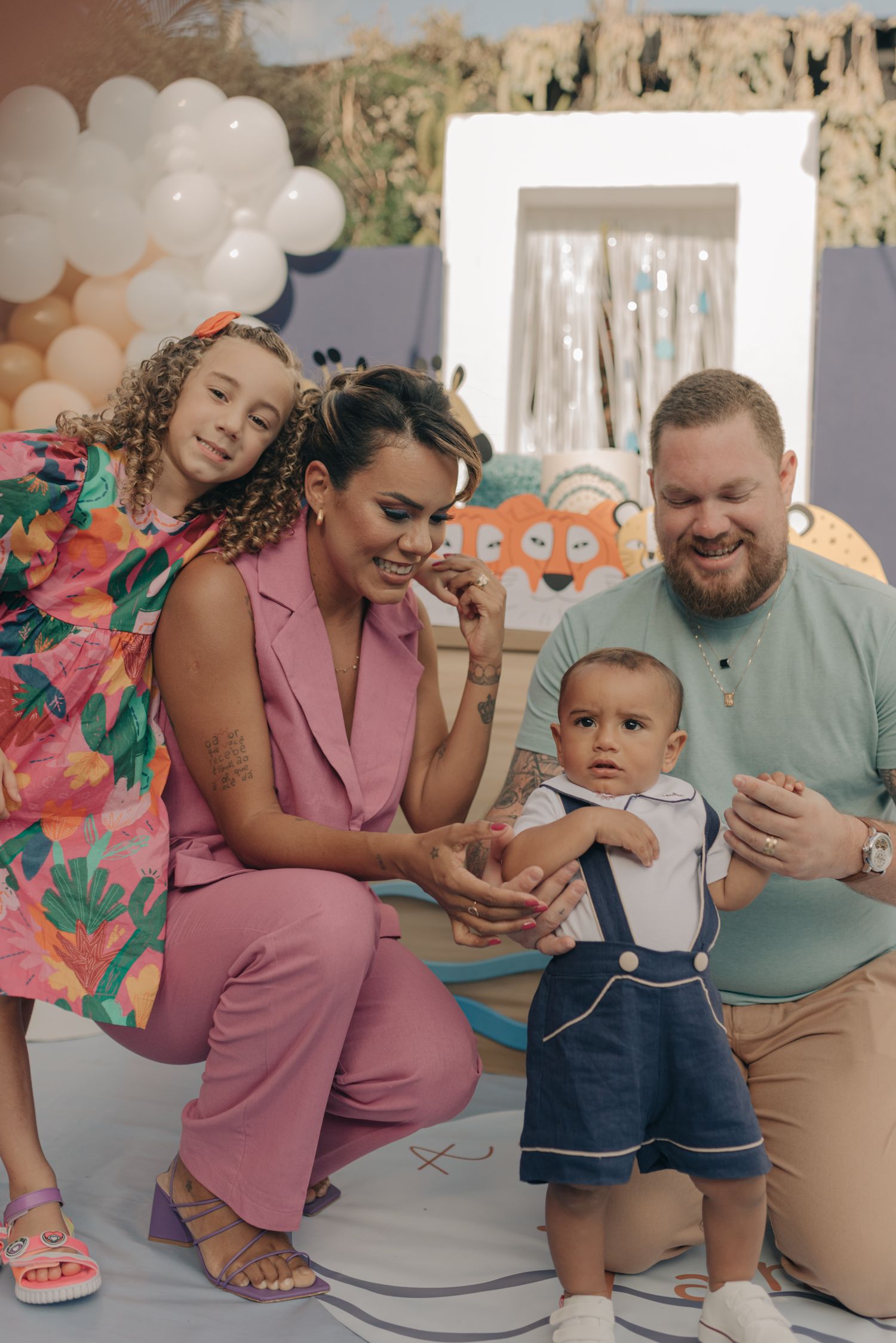 Family gathered around child at celebration with balloons and decorative backdrop.