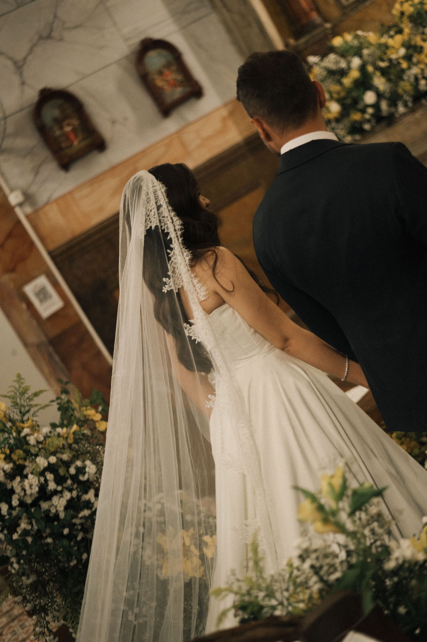 Bride and groom standing at church altar during wedding ceremony, bride wearing white gown and lace veil.