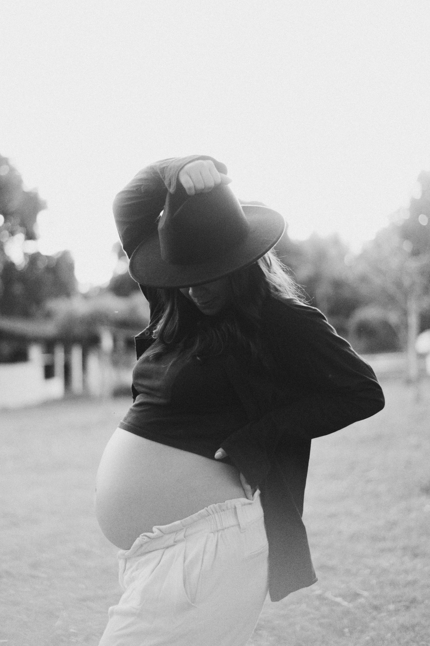 Black and white portrait of pregnant woman in hat posing in casual outdoor setting.