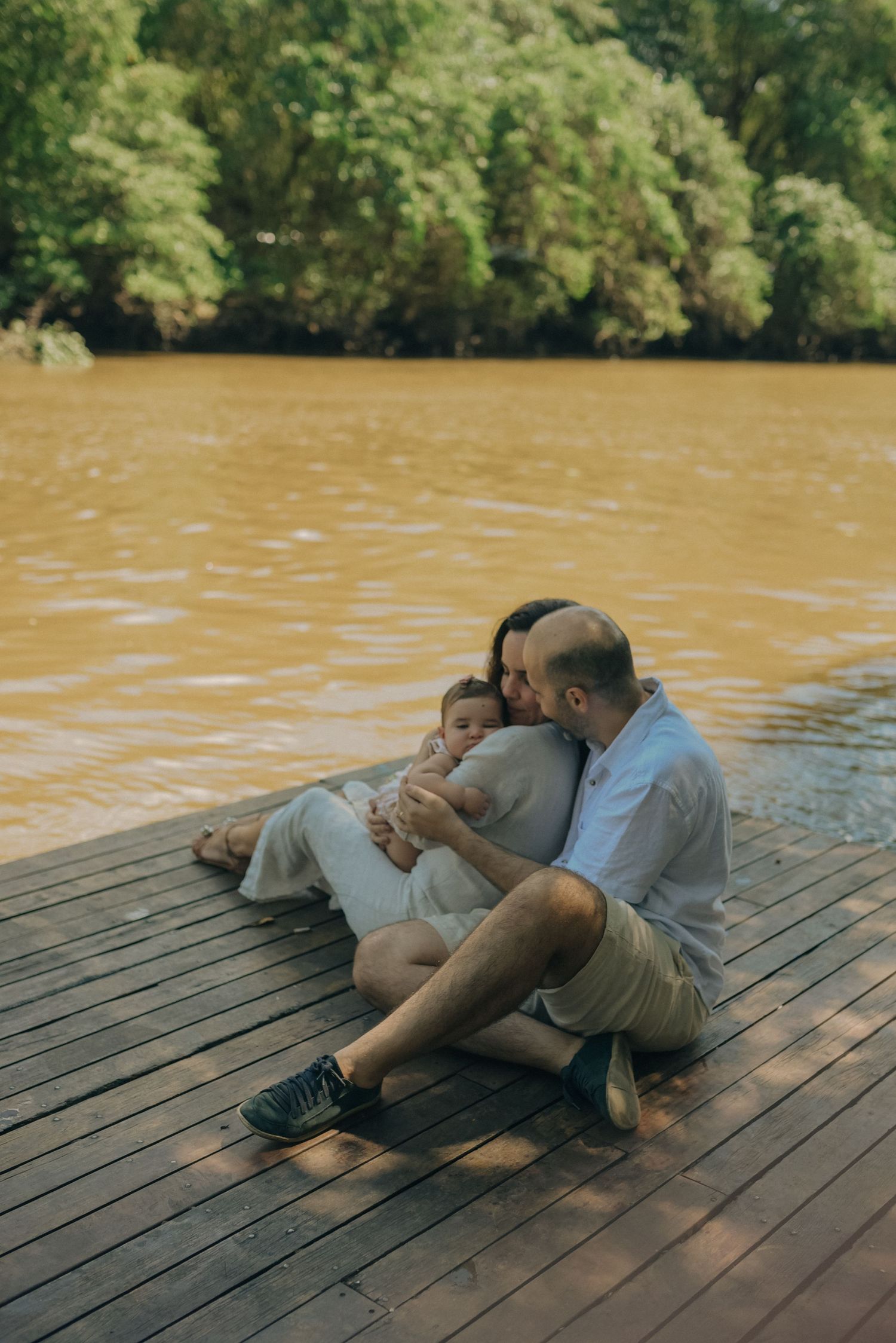 Family relaxing together on wooden dock by lake surrounded by lush green trees.