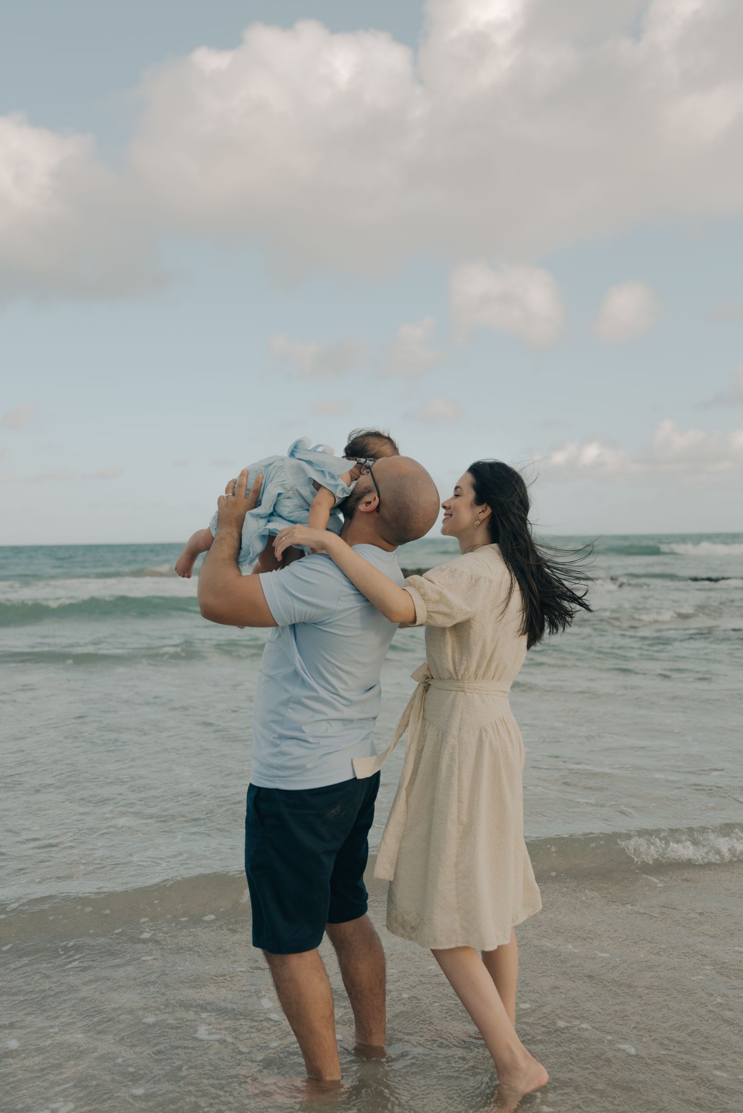 Family enjoying a playful moment together at the beach with ocean waves in the background.