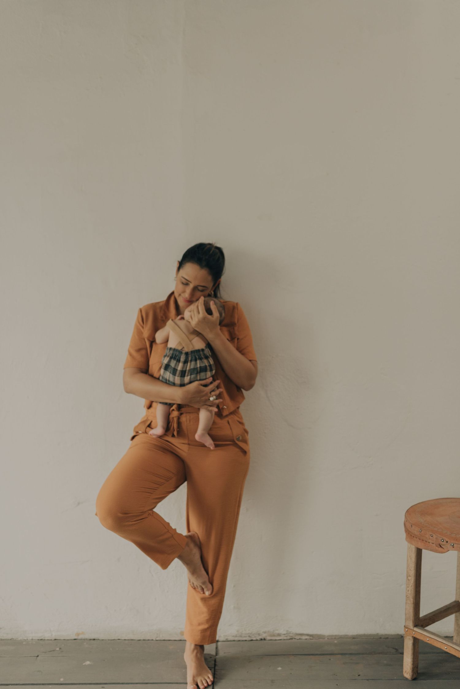 Parent in orange attire leaning against wall while holding and embracing baby.