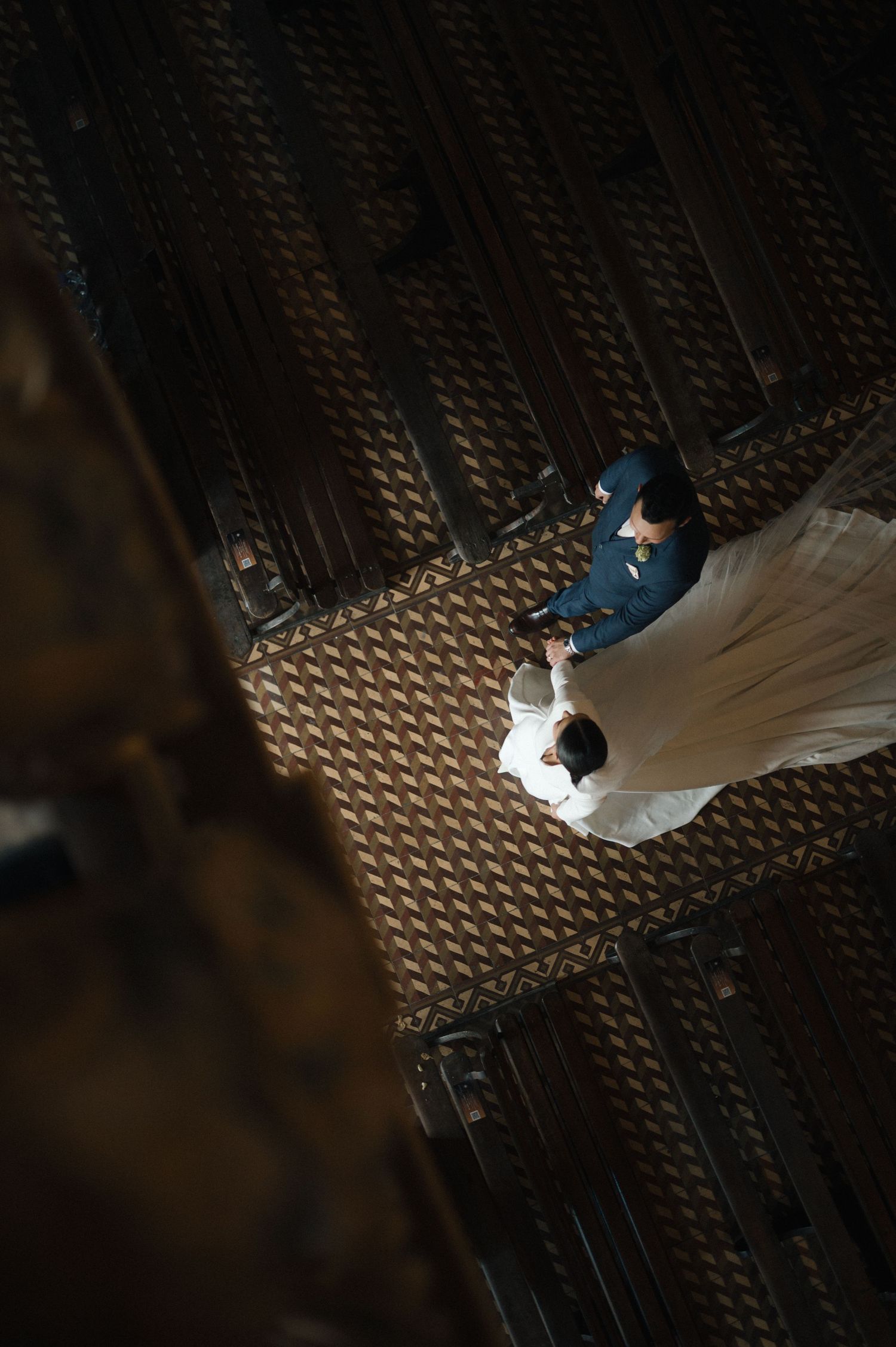 Aerial view of bride and groom holding hands on ornate patterned church floor during wedding.