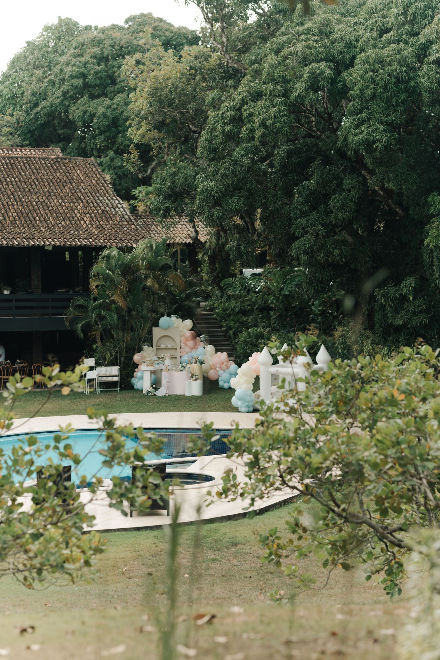 Scenic outdoor party setup with pool and vintage building surrounded by lush greenery.