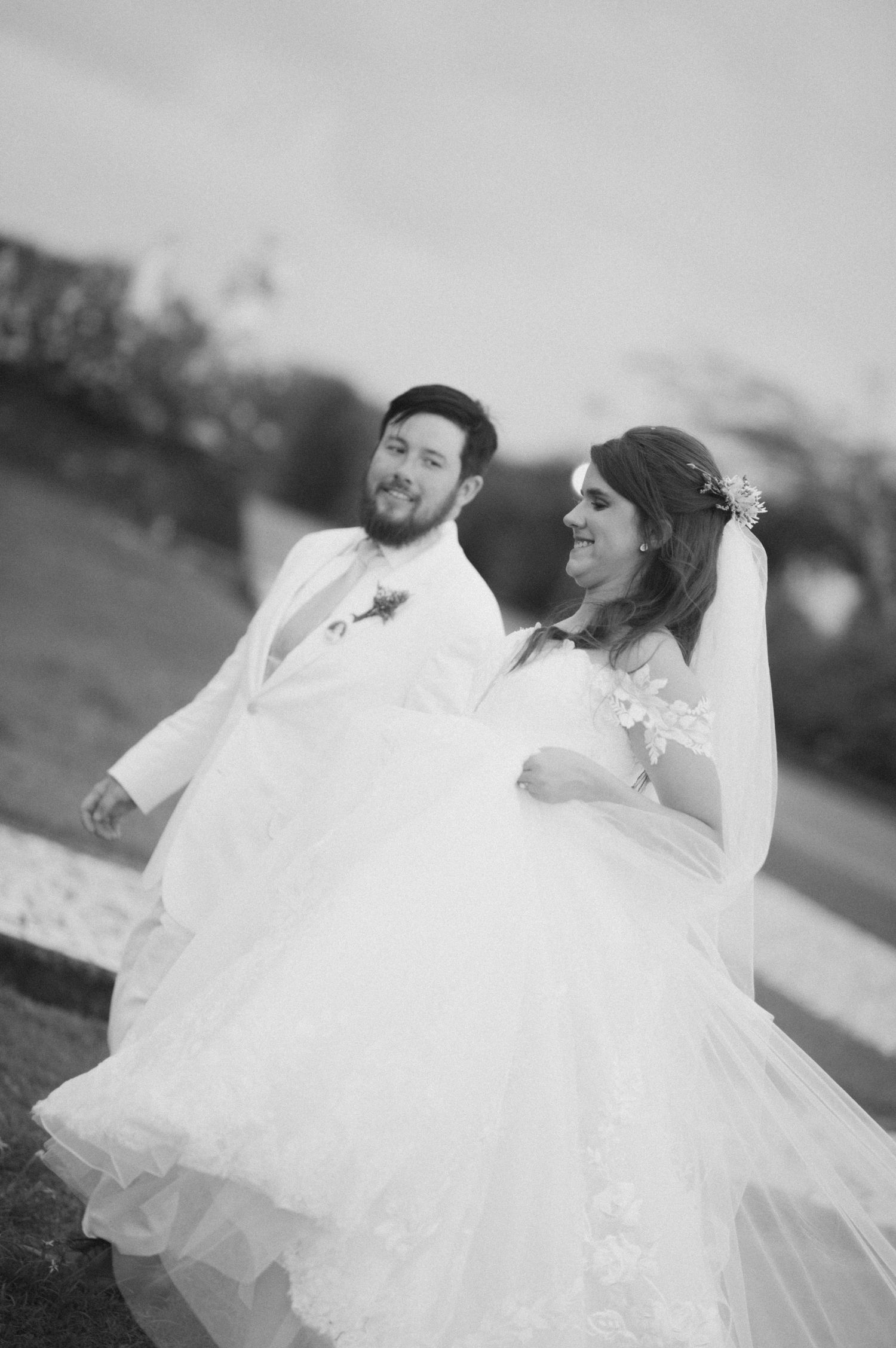 A romantic wedding portrait showing a couple in white embracing outdoors with a soft focus background.