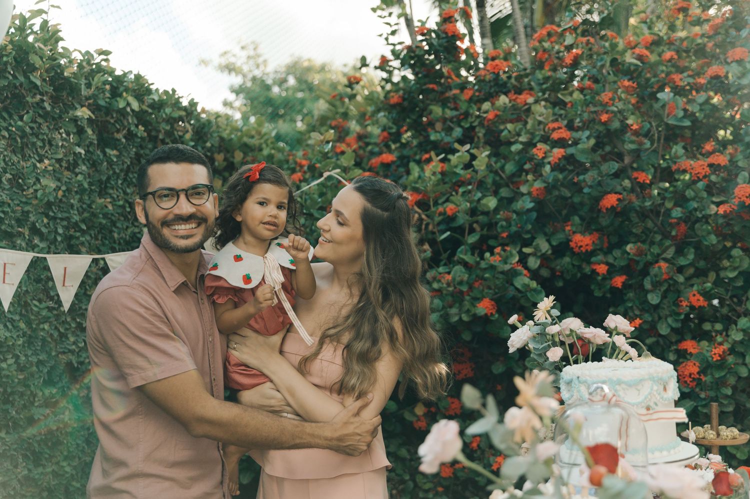 Family celebration photo with dessert table and blooming red flowers in garden setting.
