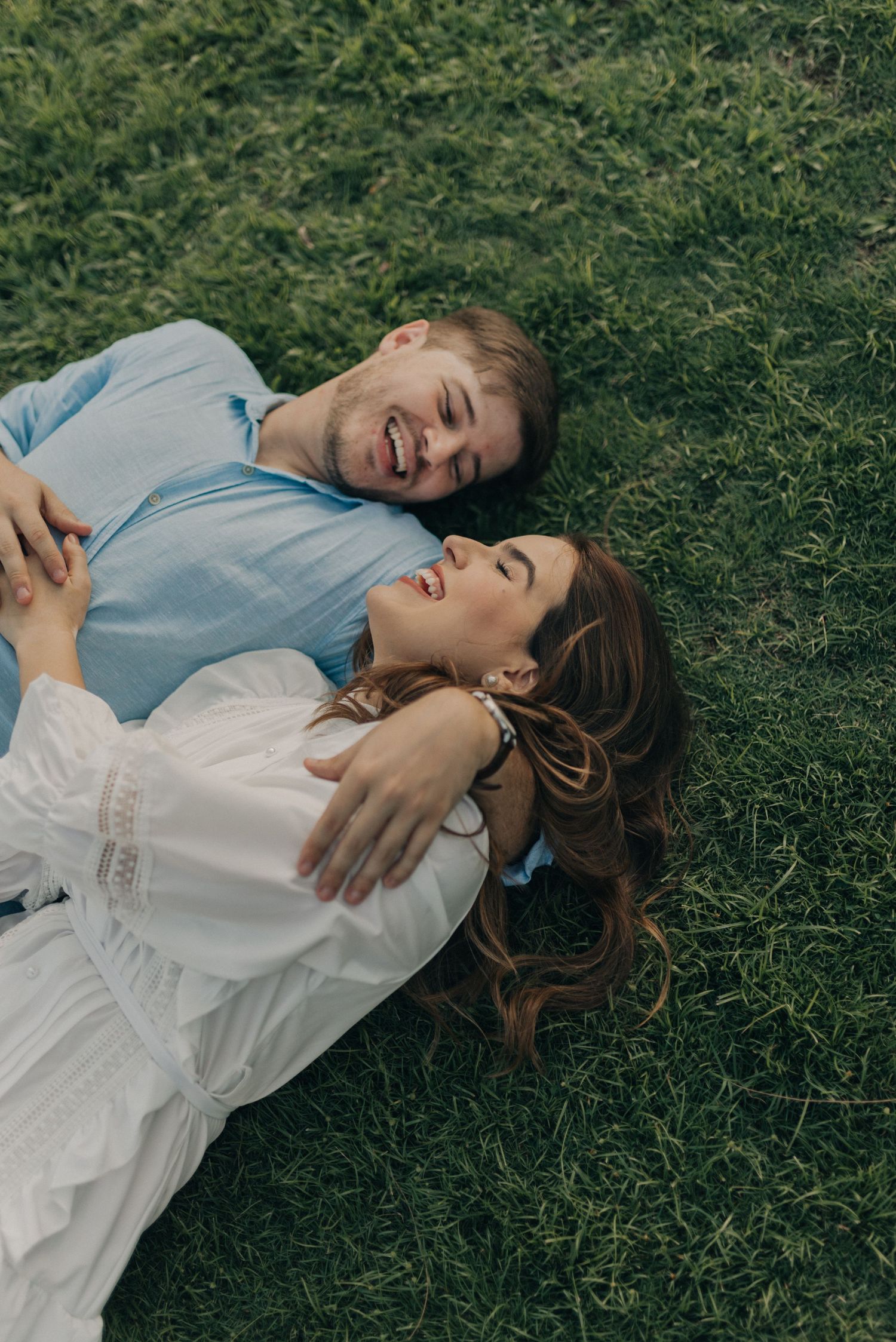 Happy couple lying on green grass and laughing together outdoors.