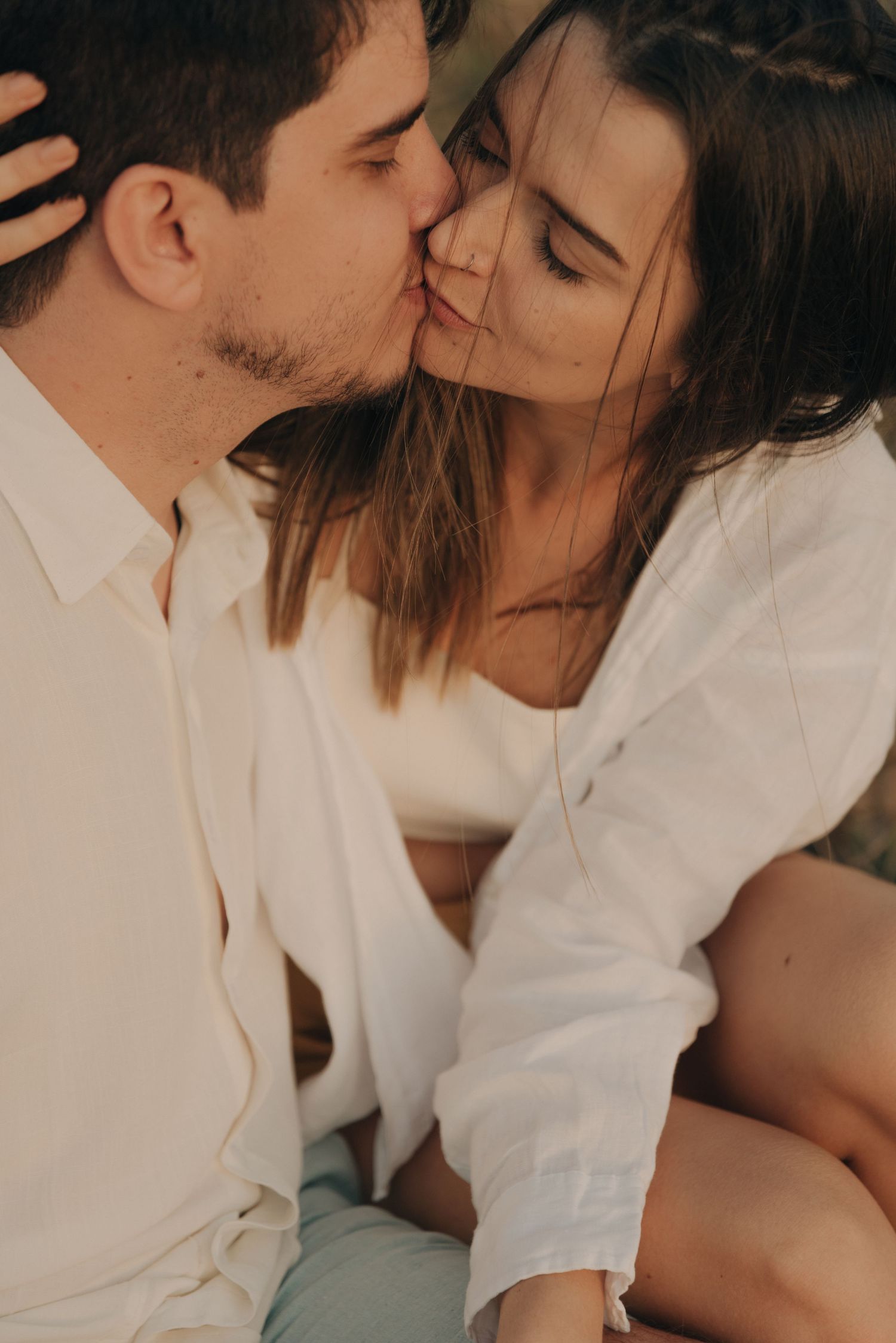 A tender moment between a couple in white clothing during an outdoor photoshoot.