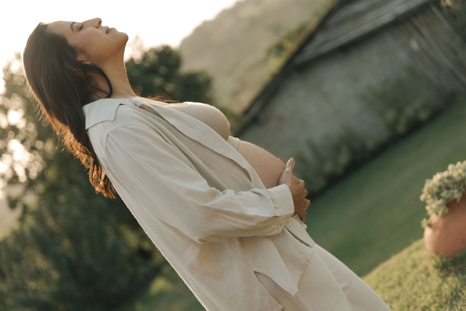 Ethereal outdoor maternity photo of expecting mother in flowing white dress at sunset.